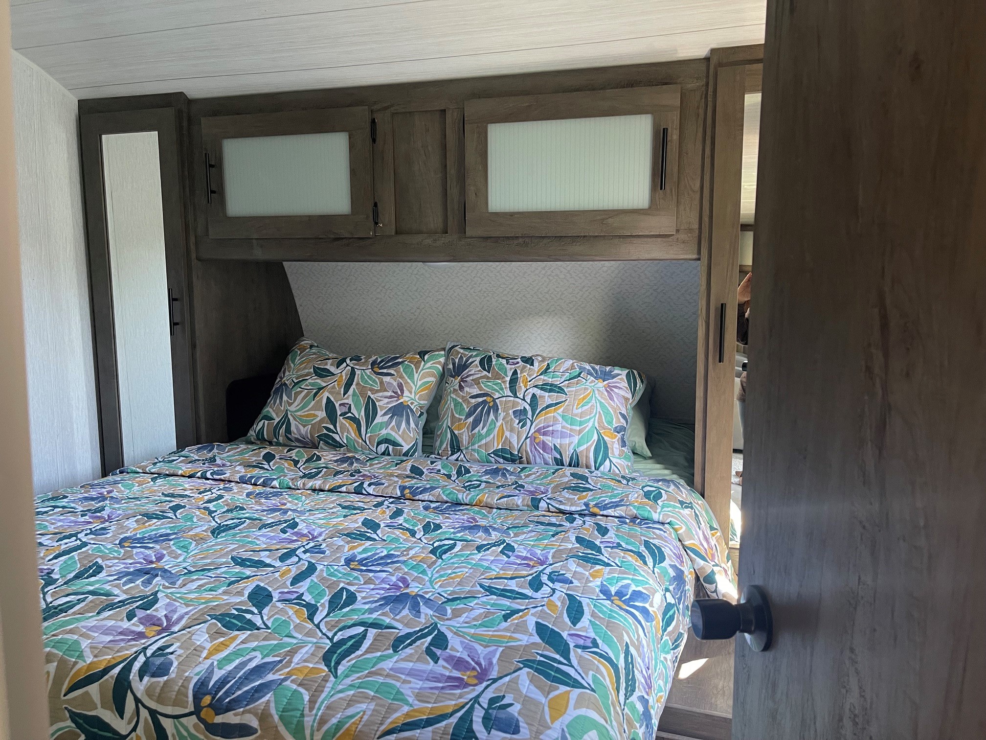 Cozy RV rental bedroom featuring a colorful floral bedspread, overhead storage, and a mirrored wardrobe.. Forest River Salem 2022