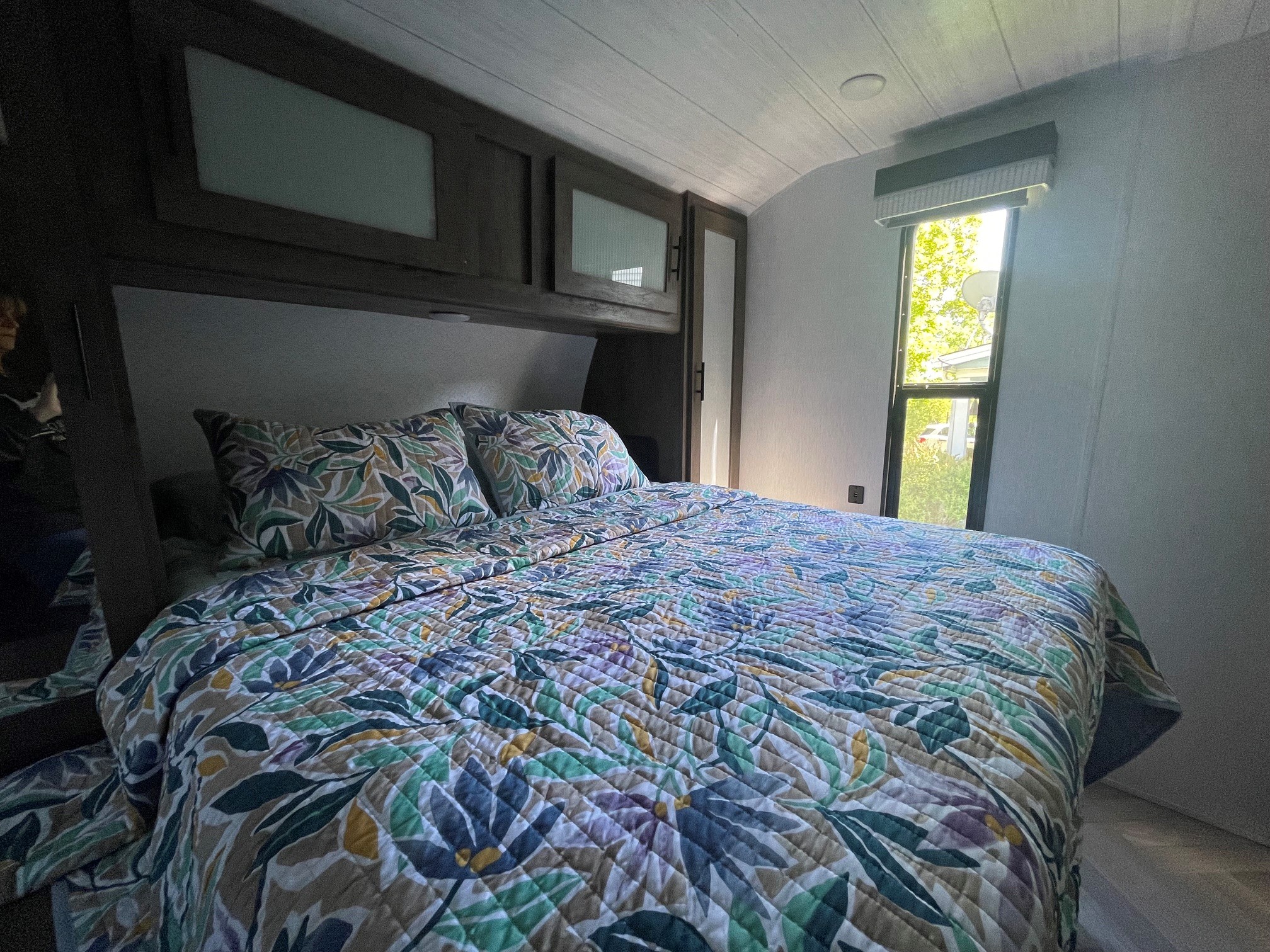 This rv rental bedroom offers a comfortable bed with a vibrant floral quilt, overhead storage, and a sunlit window.. Forest River Salem 2022