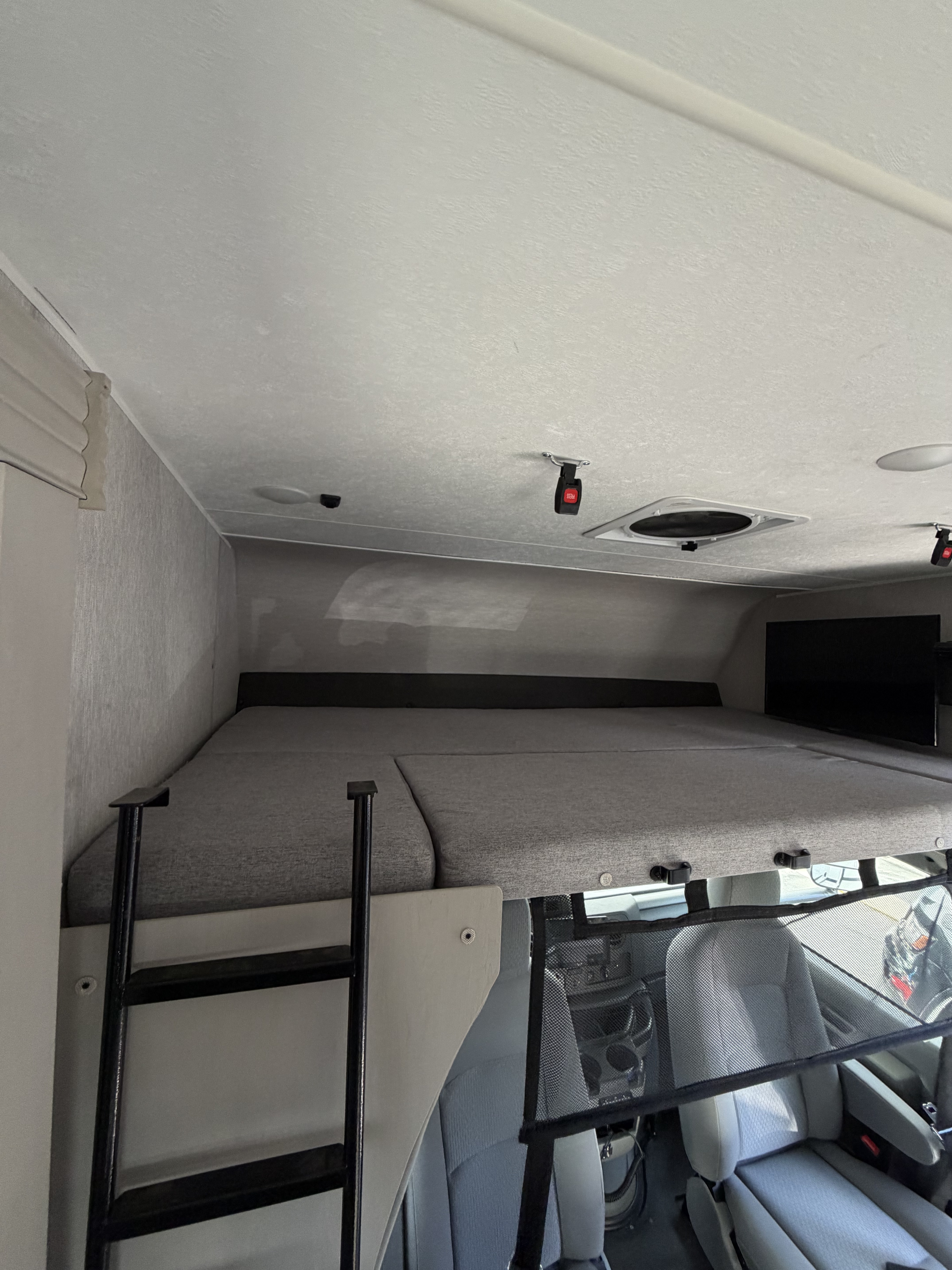 View inside an RV rental: gray cab-over bunk bed with ladder, safety net, TV, and driver's area below.. Forest River Coachmen Freelander 2023