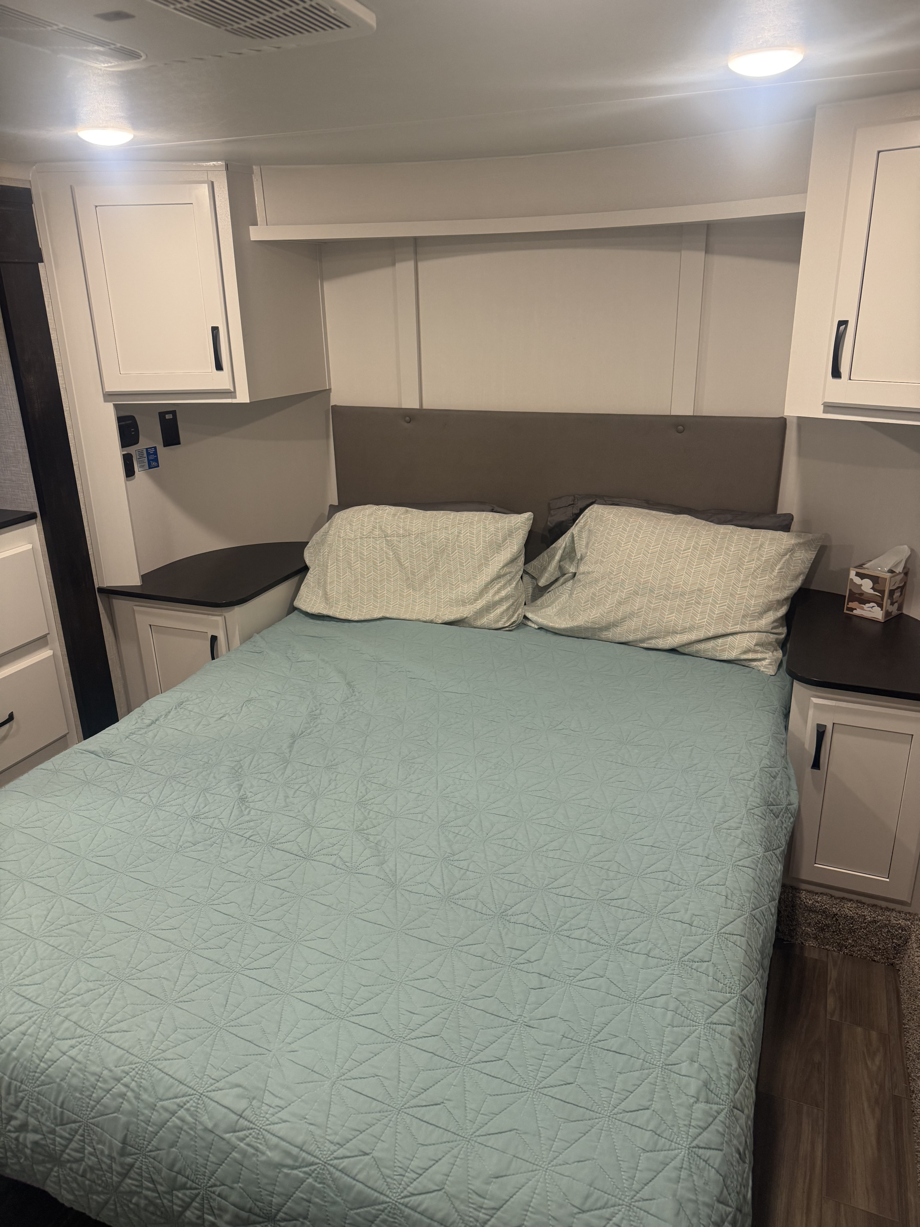Comfortable rv rental bedroom interior with a headboard, bed, soft blue quilt, pillows, and white storage cabinets overhead.. Jayco Seismic Toy Hauler 2024