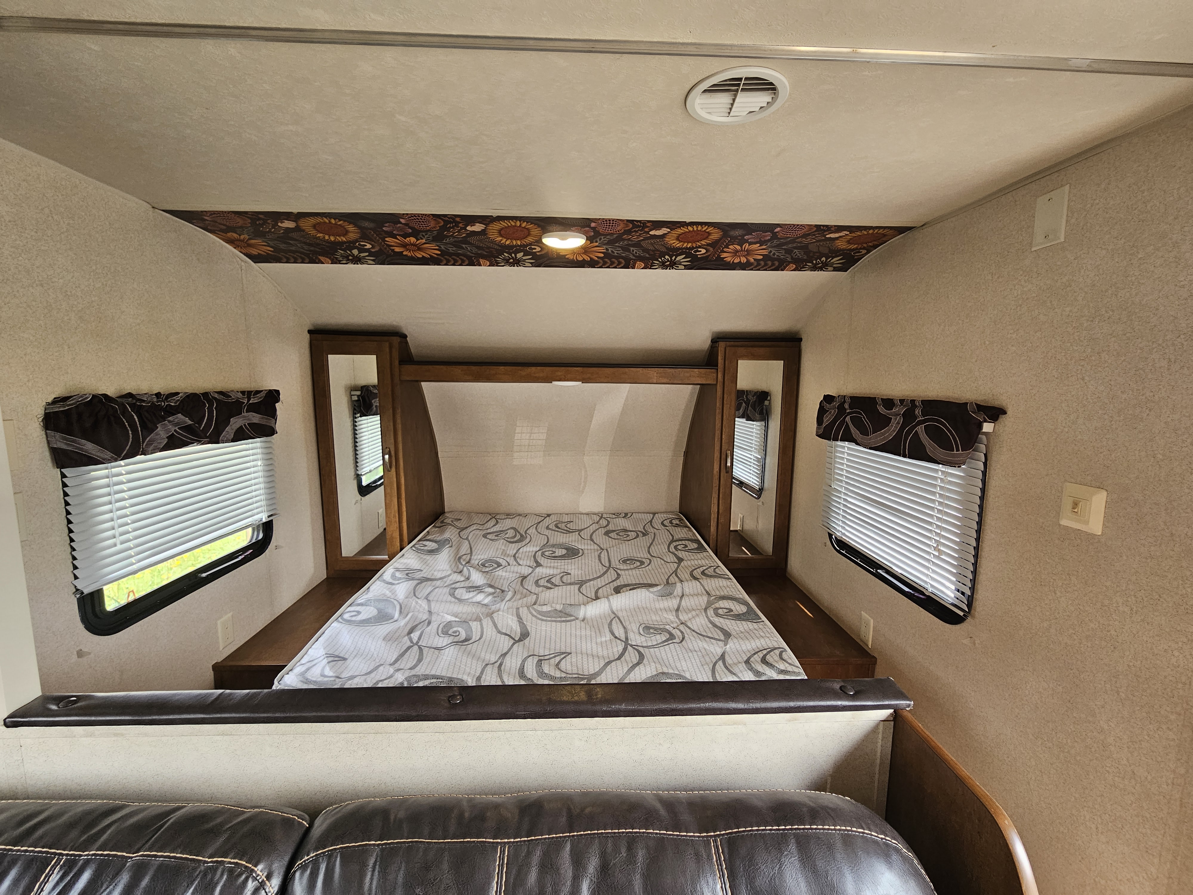 Cozy RV rental bedroom interior with a patterned bed, mirrored storage, and windows, viewed from the living area.. Forest River Salem Cruise Lite 2017
