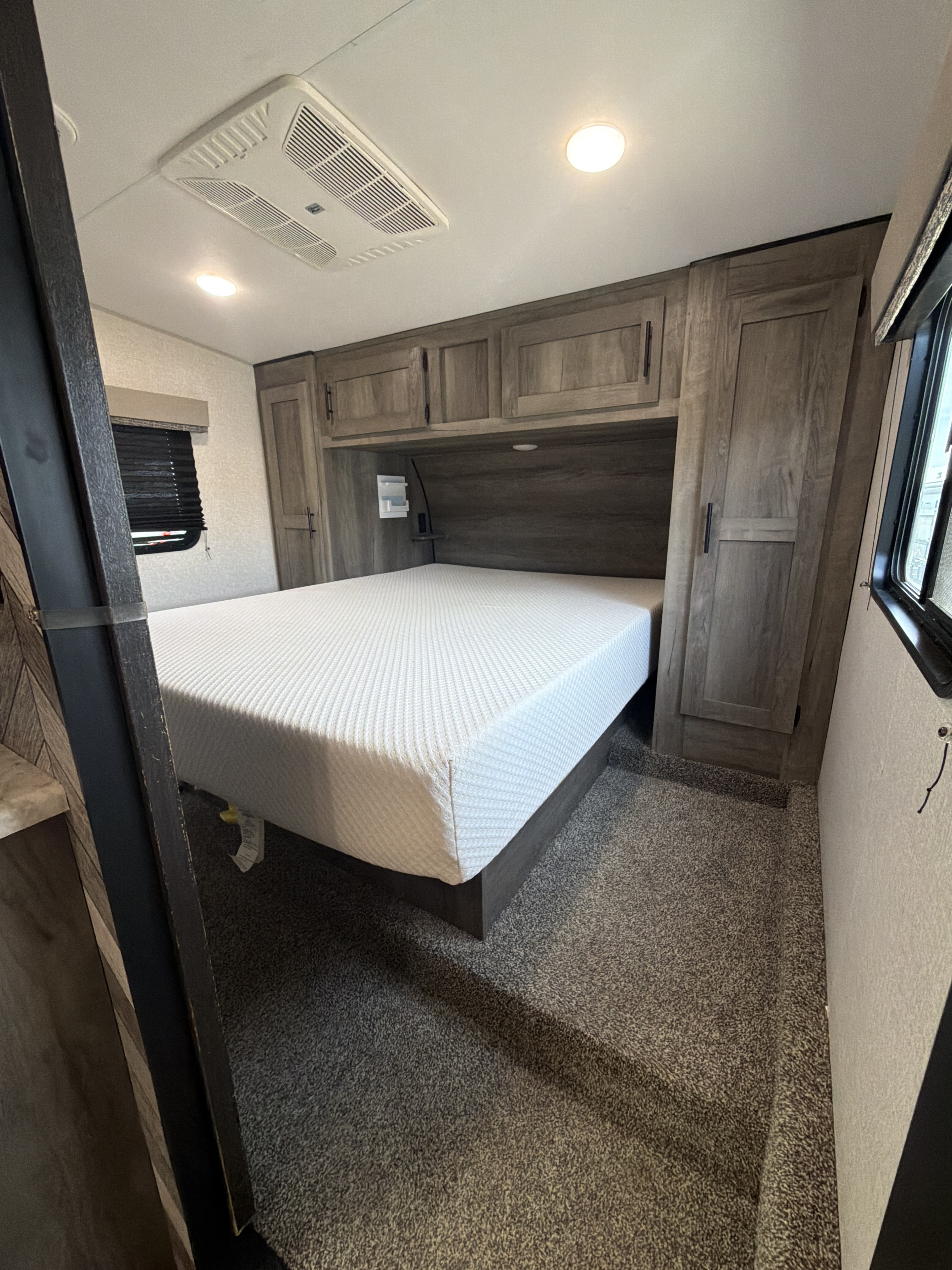 Inside an RV rental bedroom: a large bed, wood-grain storage cabinets, and overhead AC unit ensure a comfortable journey.. KZ 331th13 2021