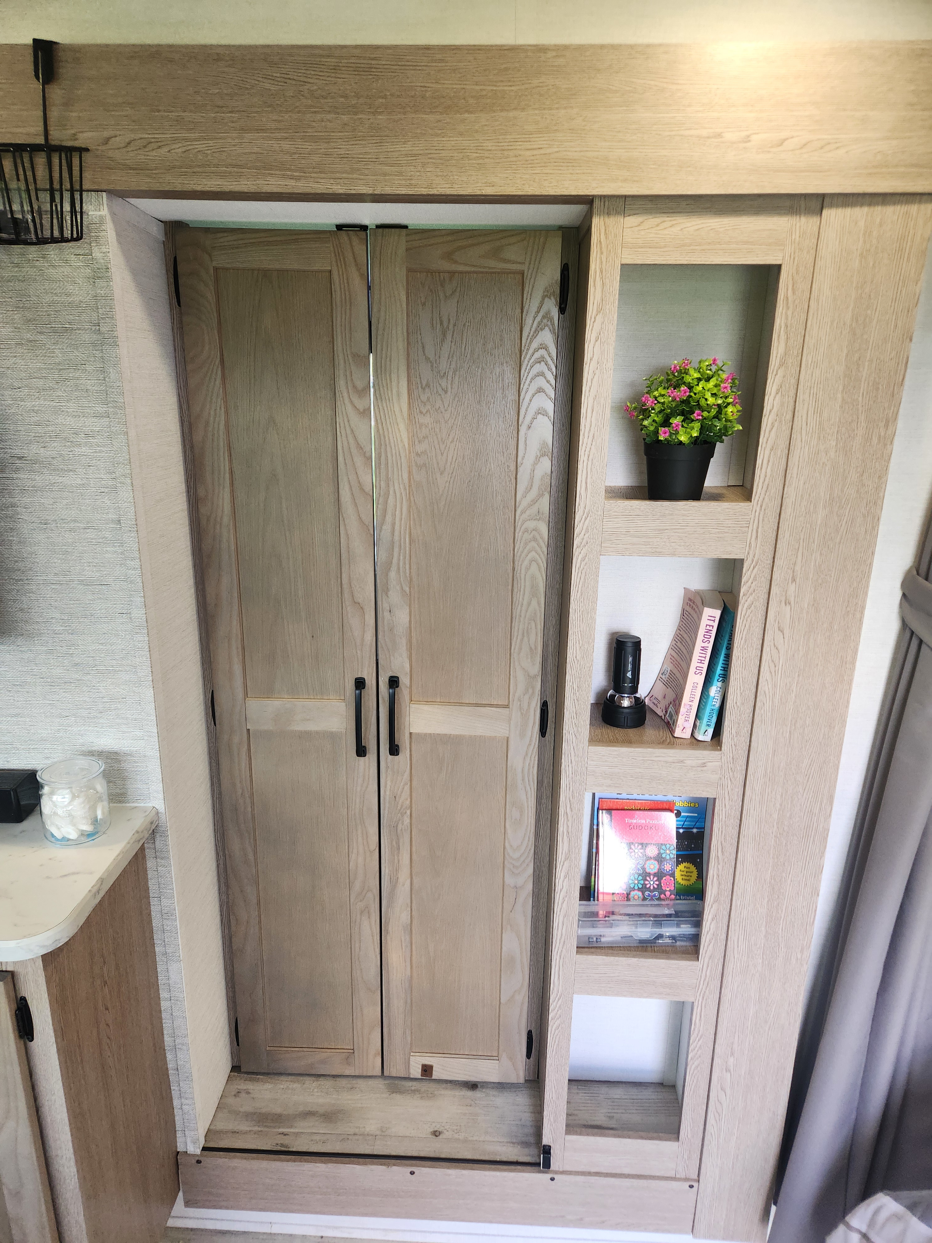 RV rental interior showcasing light wood doors and integrated shelves with decor, books. Functional compact storage.. Gulf stream Grand river 2026
