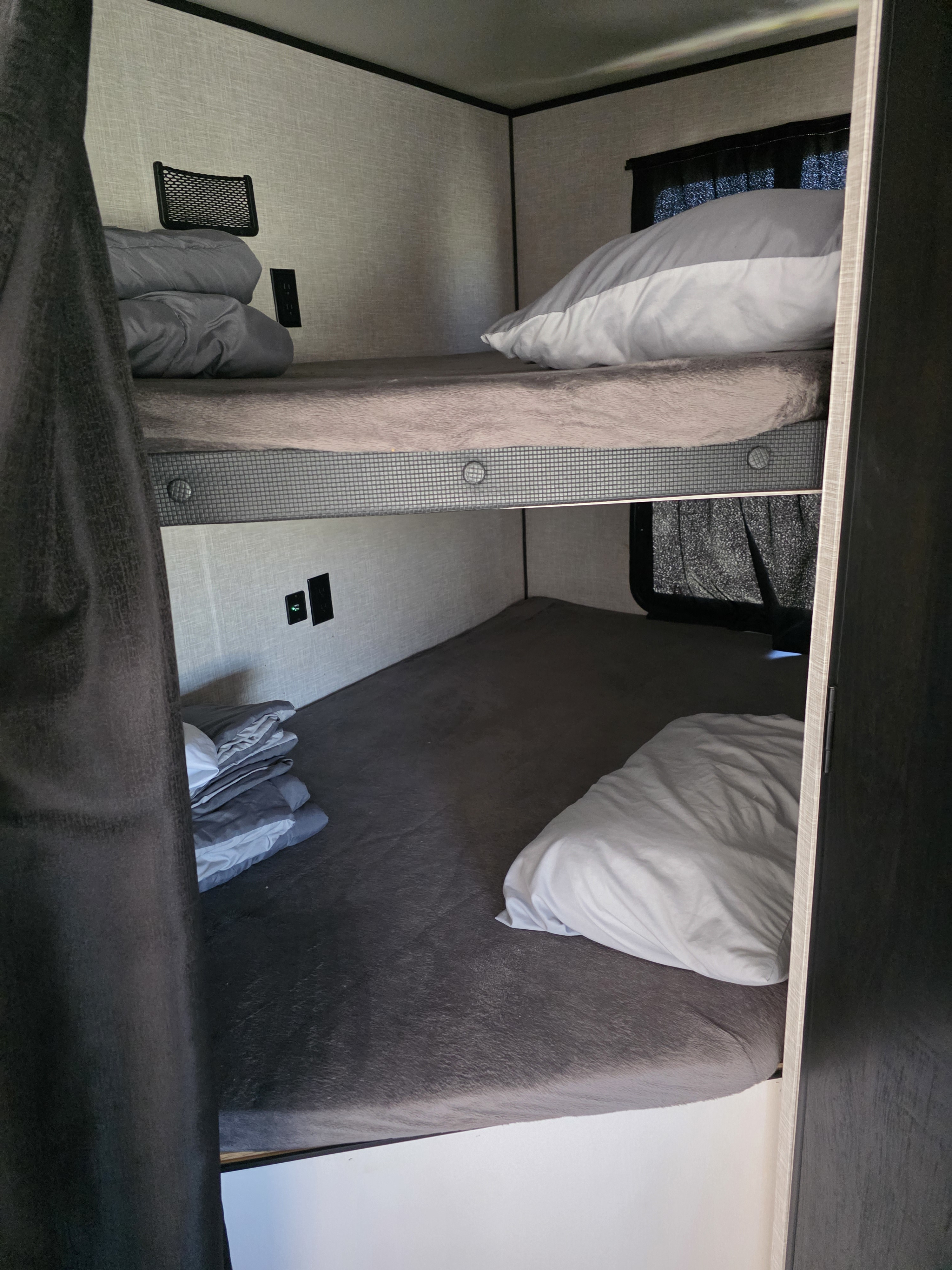 Cozy RV rental bunk beds with grey bedding, pillows, power outlets, and a storage net.. Highland Ridge RV Open Range 2022