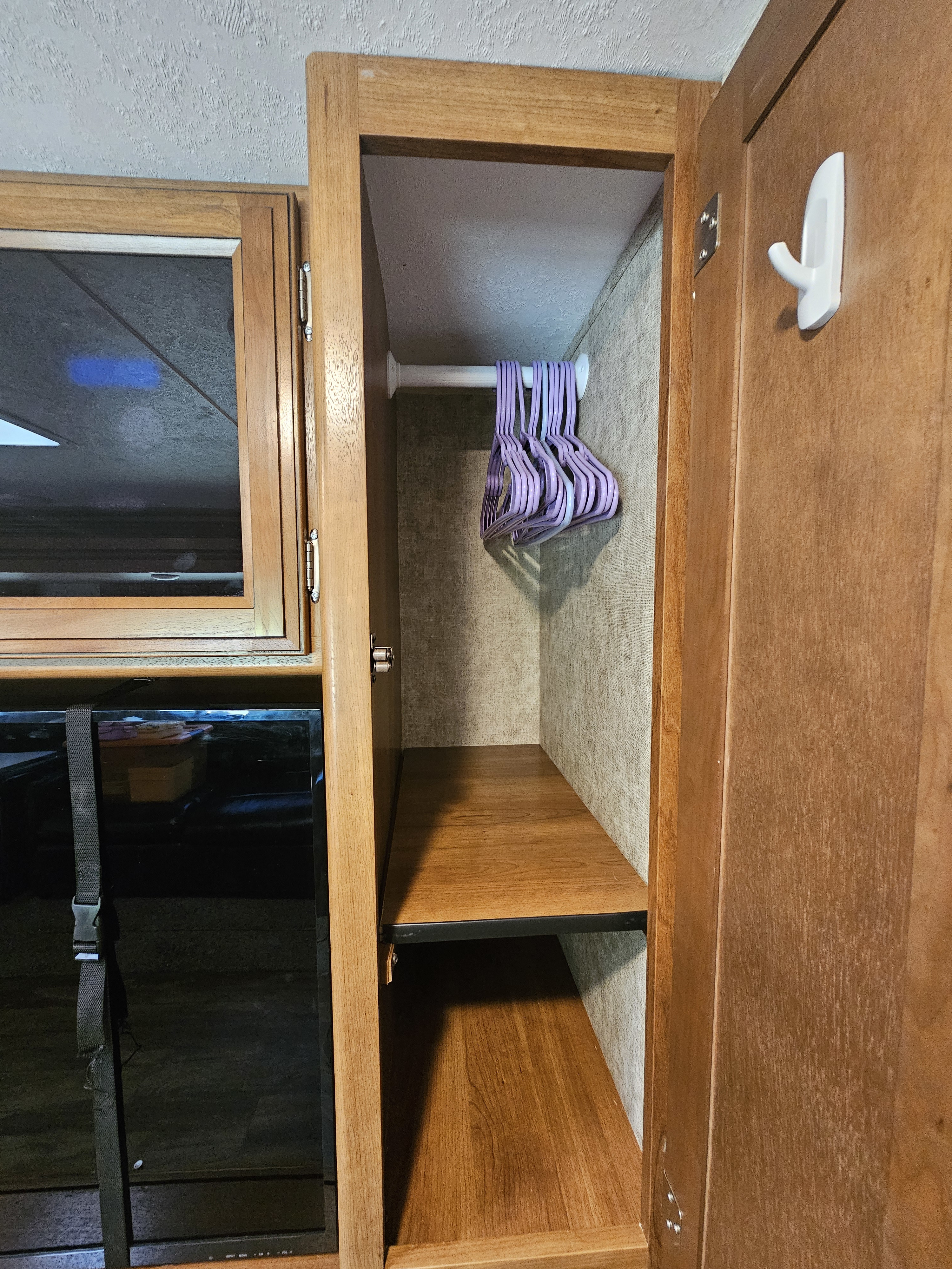 Compact rv rental wardrobe features a hanging rod with purple hangers, two storage shelves, and a secured TV for organized living.. Forest River Tracer Air 2018