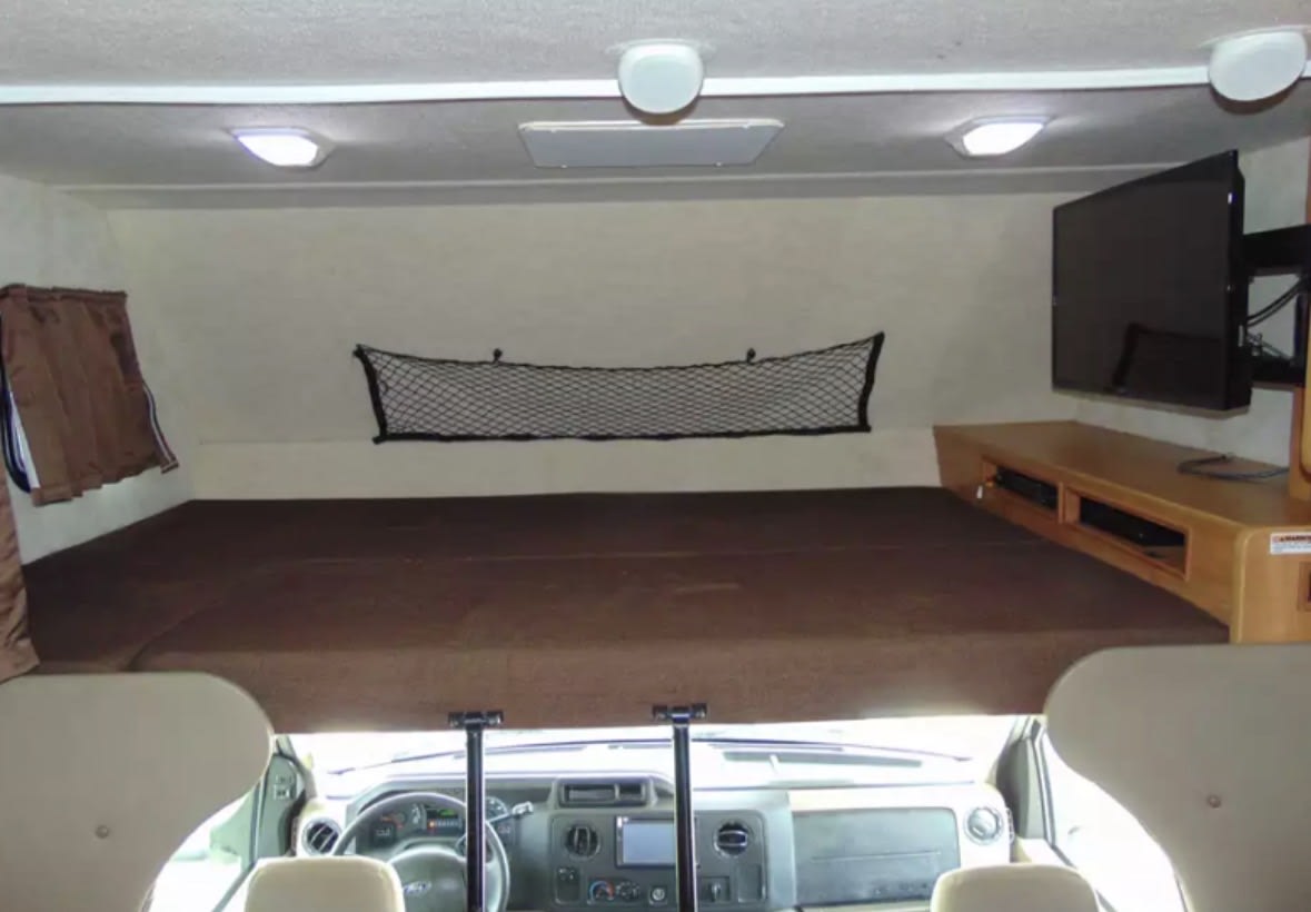 RV rental's over-cab bed area features a comfy mattress, TV entertainment, and cargo net storage. Driver's dash visible below.. Tioga Ranger 2012