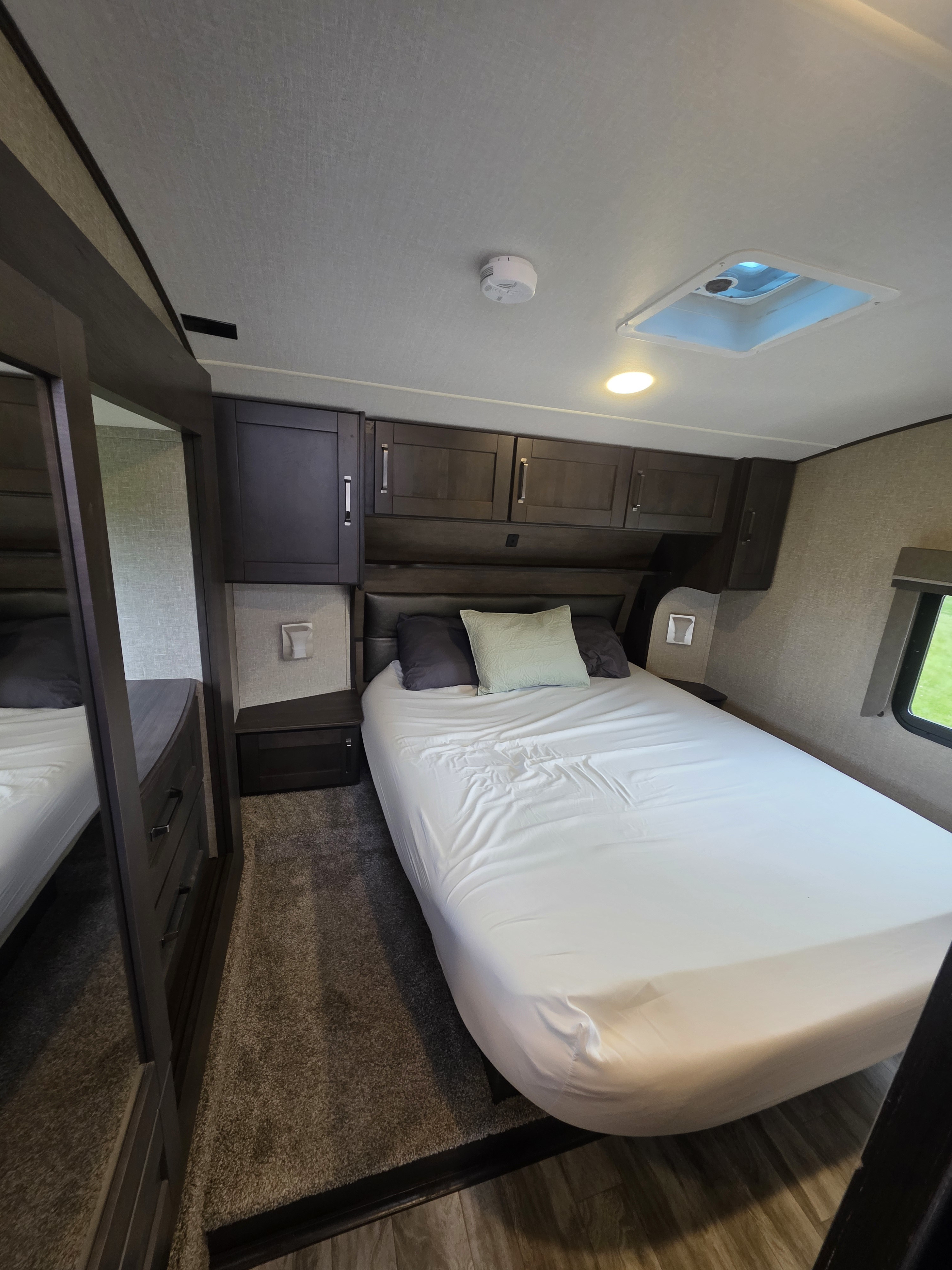 Inviting RV rental bedroom with a comfortable bed, dark wood storage, mirrored wardrobe, window, and ceiling features.. Grand Design Reflection 2022