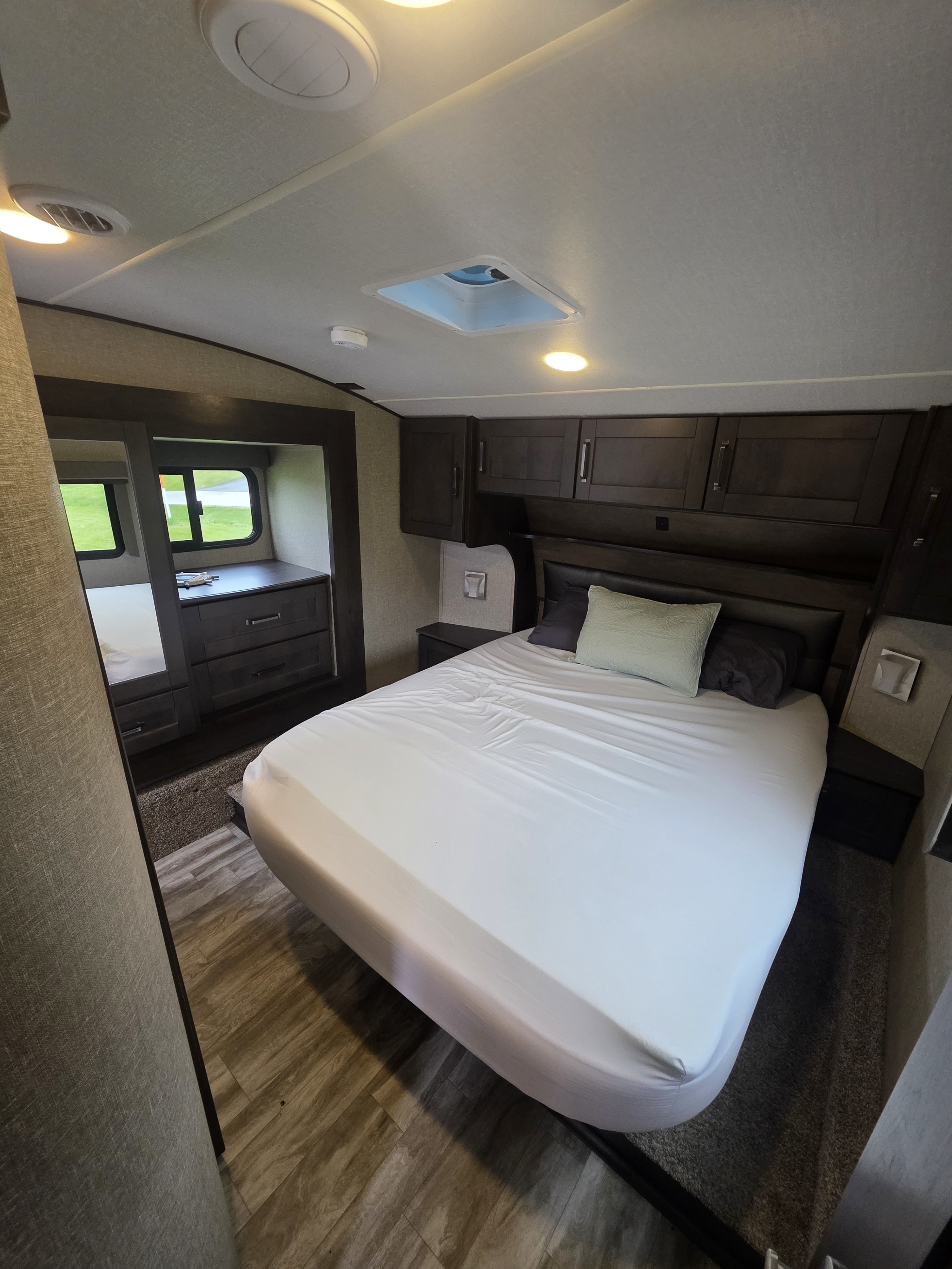 RV rental bedroom with a comfortable bed, overhead cabinets, and a dresser, offering a cozy sleeping space.. Grand Design Reflection 2022