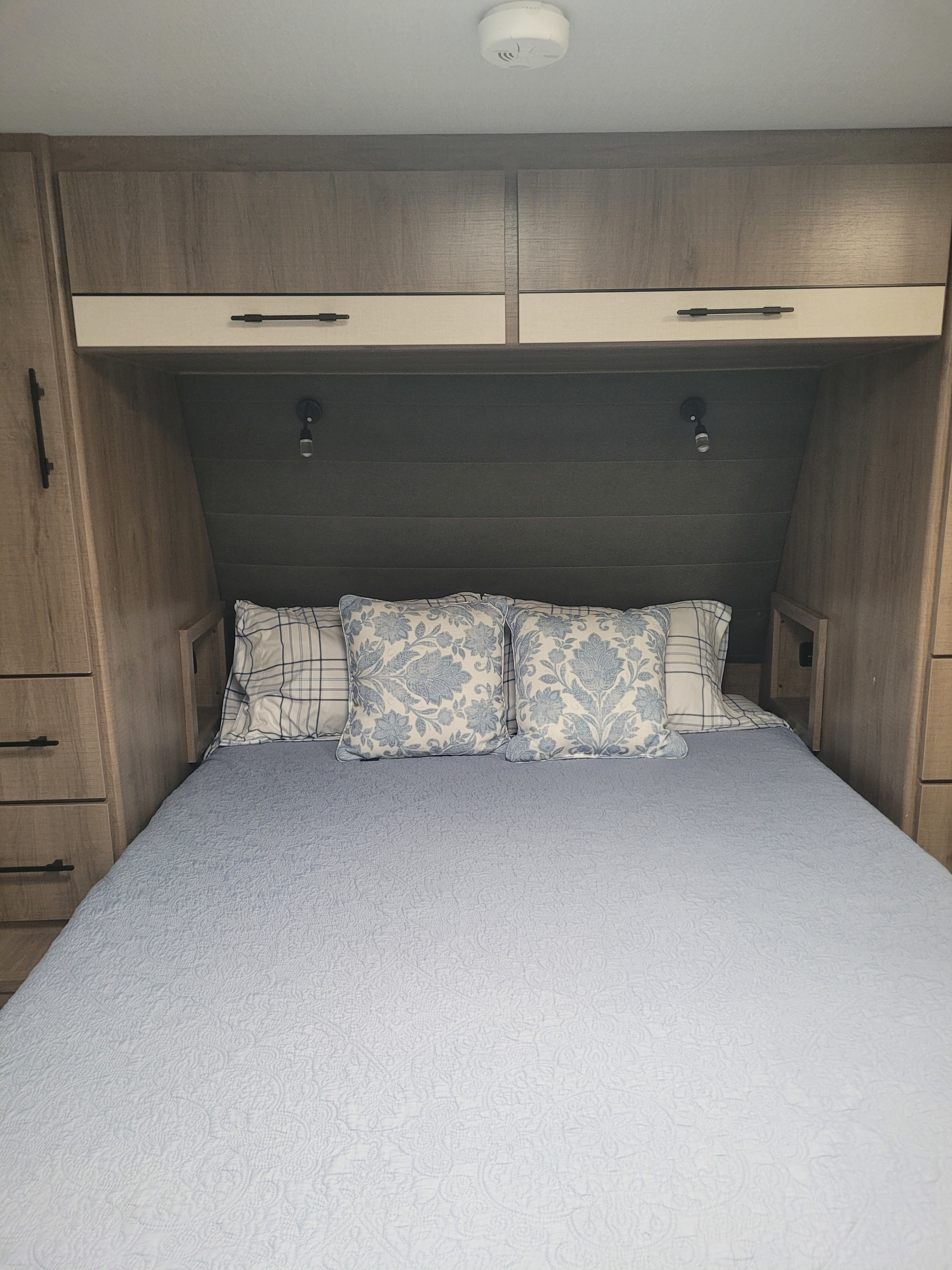 Relax in this RV rental bedroom: blue bed, patterned pillows, integrated cabinets, and reading lights.. Grand Design Imagine XLS 2023