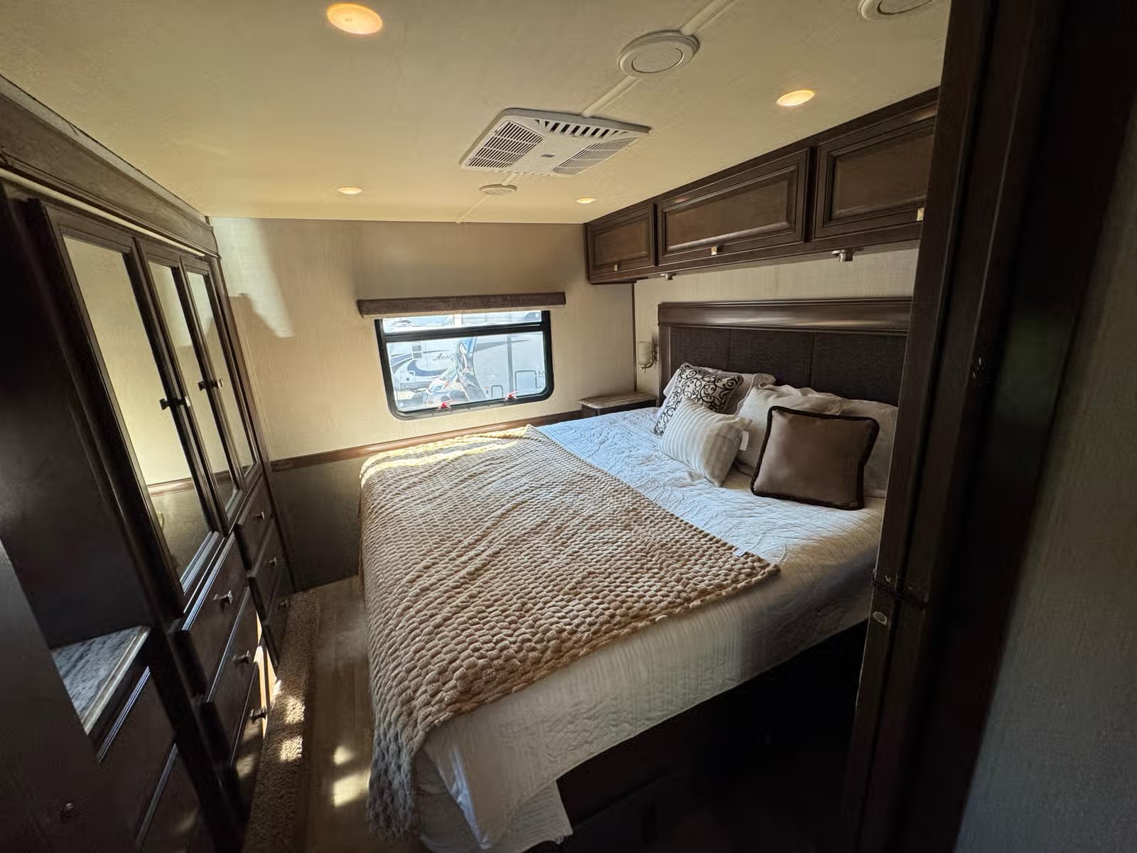 Cozy RV rental bedroom features a comfortable bed, overhead cabinets, and a window for scenic views, ensuring a relaxing travel experience.. Holiday Rambler Admiral 2019