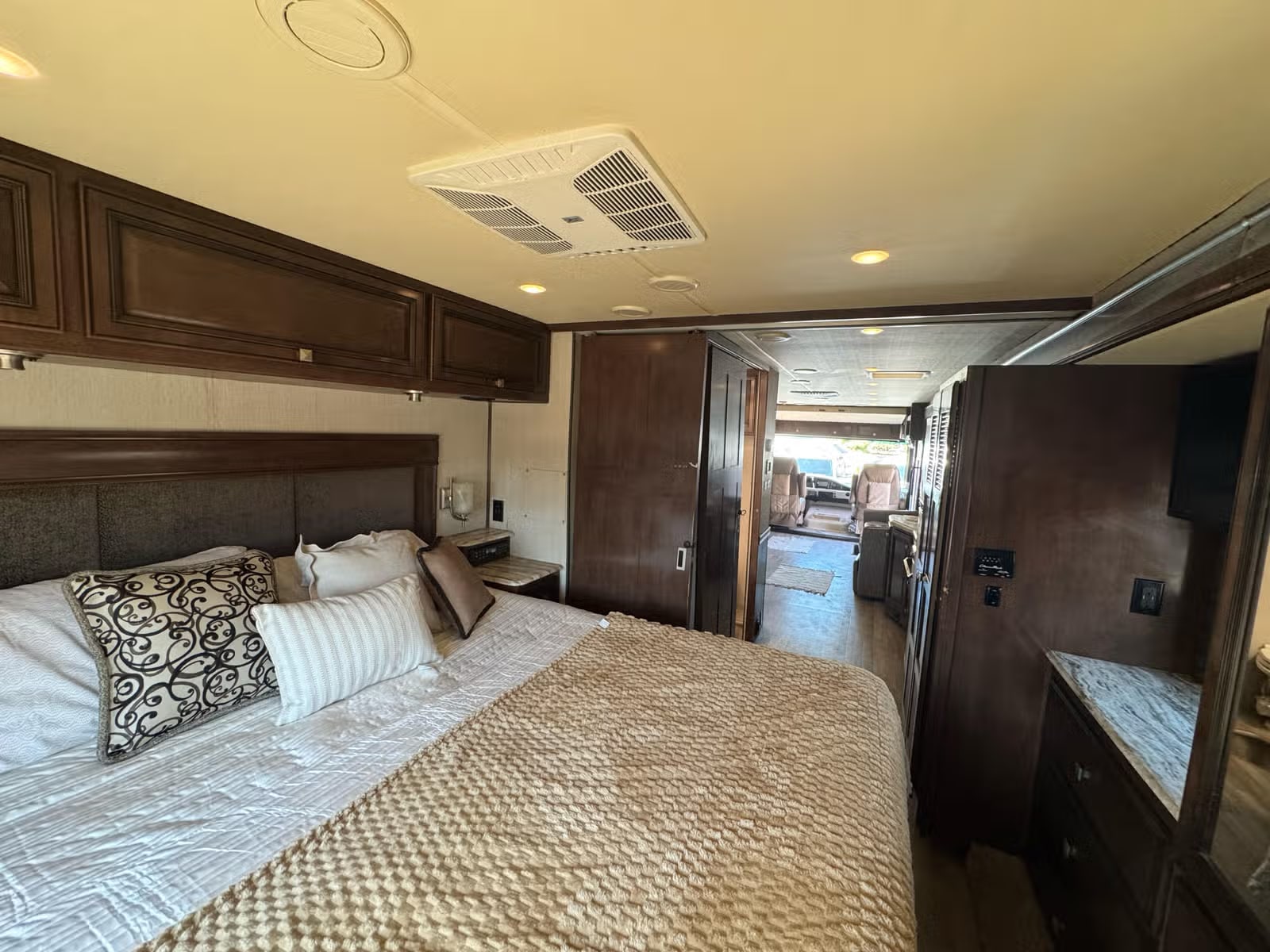 Step inside this RV rental! A cozy bedroom with dark wood finishes, plush bedding, and overhead storage for comfortable travel.. Holiday Rambler Admiral 2019