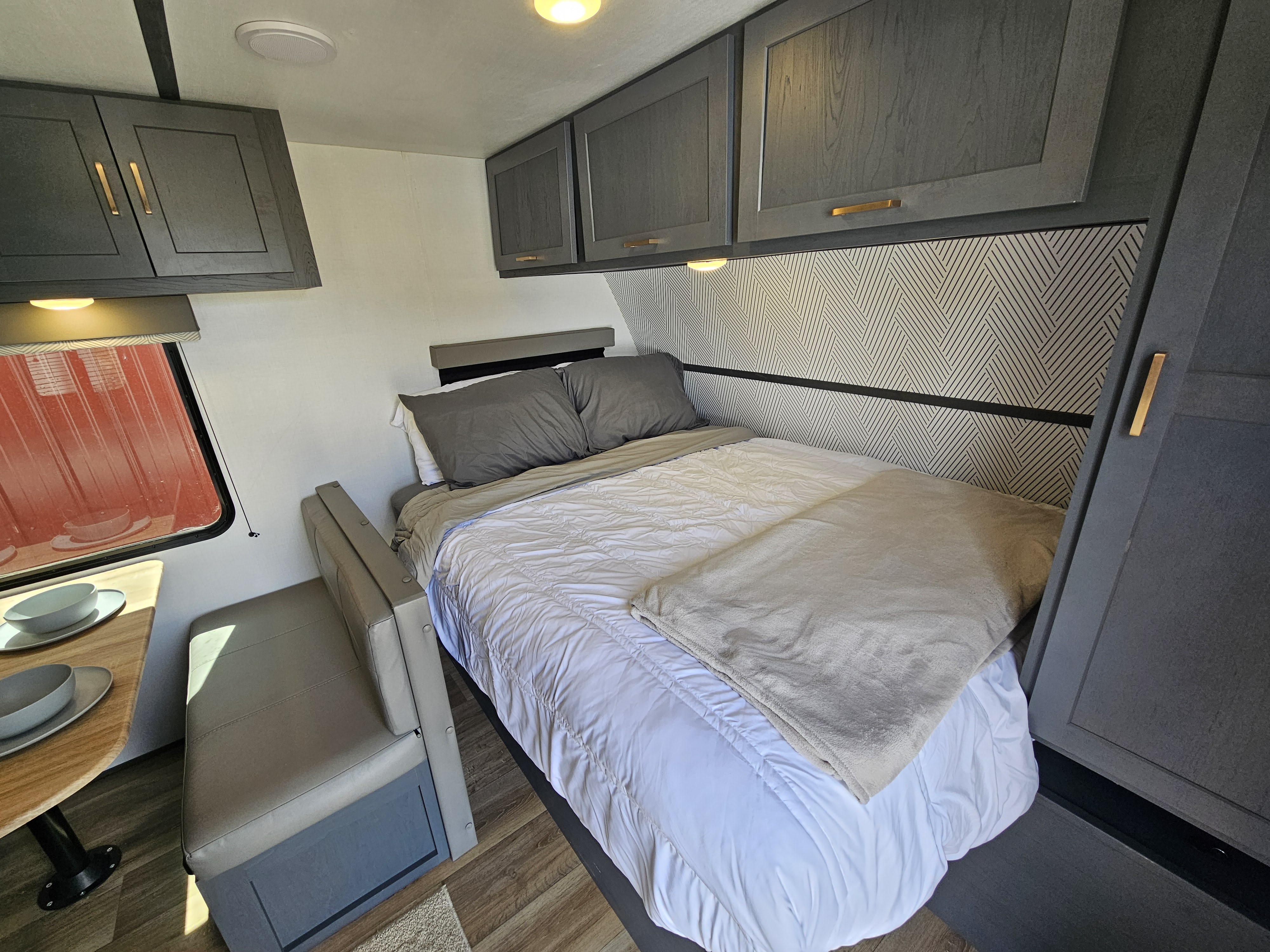 RV rental interior: modern bedroom with patterned wall, gray cabinets, cozy bed, and dining nook. Compact and stylish design.. Keystone RV Bullet Crossfire 2022
