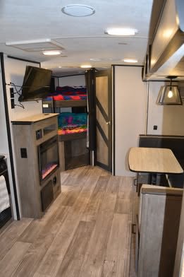 Modern RV rental interior showing a living area with TV, fireplace, dining table, and bunk beds in the back.. Heartland RVs North Trail 2022
