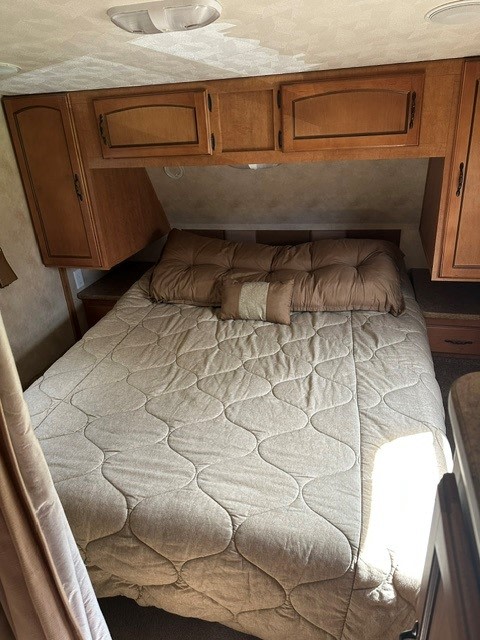 Comfortable RV rental bedroom with a queen bed, quilted comforter, pillows, and overhead wooden cabinets for storage.. Forest River Puma 2011
