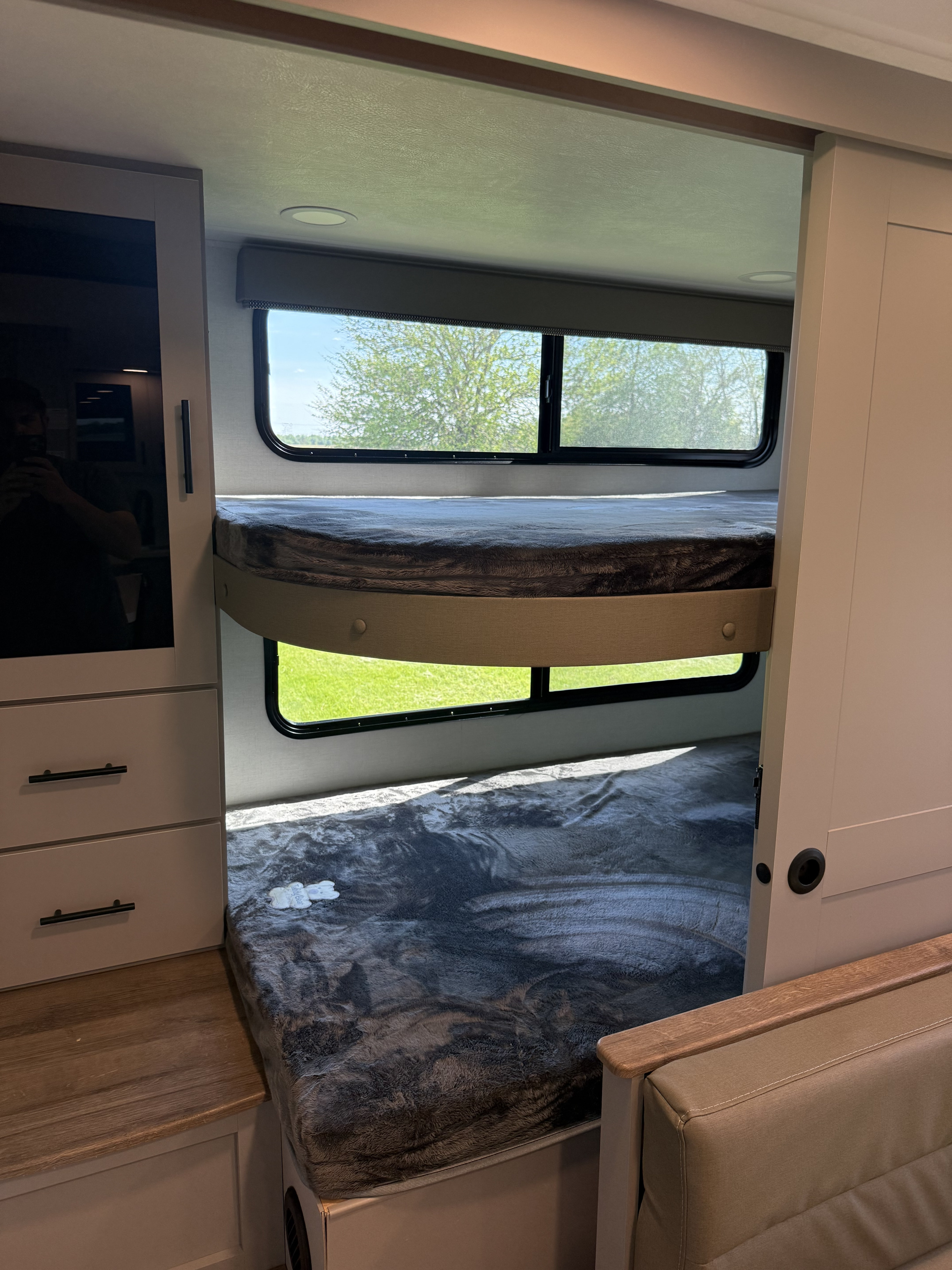 RV rental bunk beds feature cozy blankets, natural light from windows overlooking a green landscape, and adjacent cabinetry with a sliding door.. Alliance Delta 291BH 2026