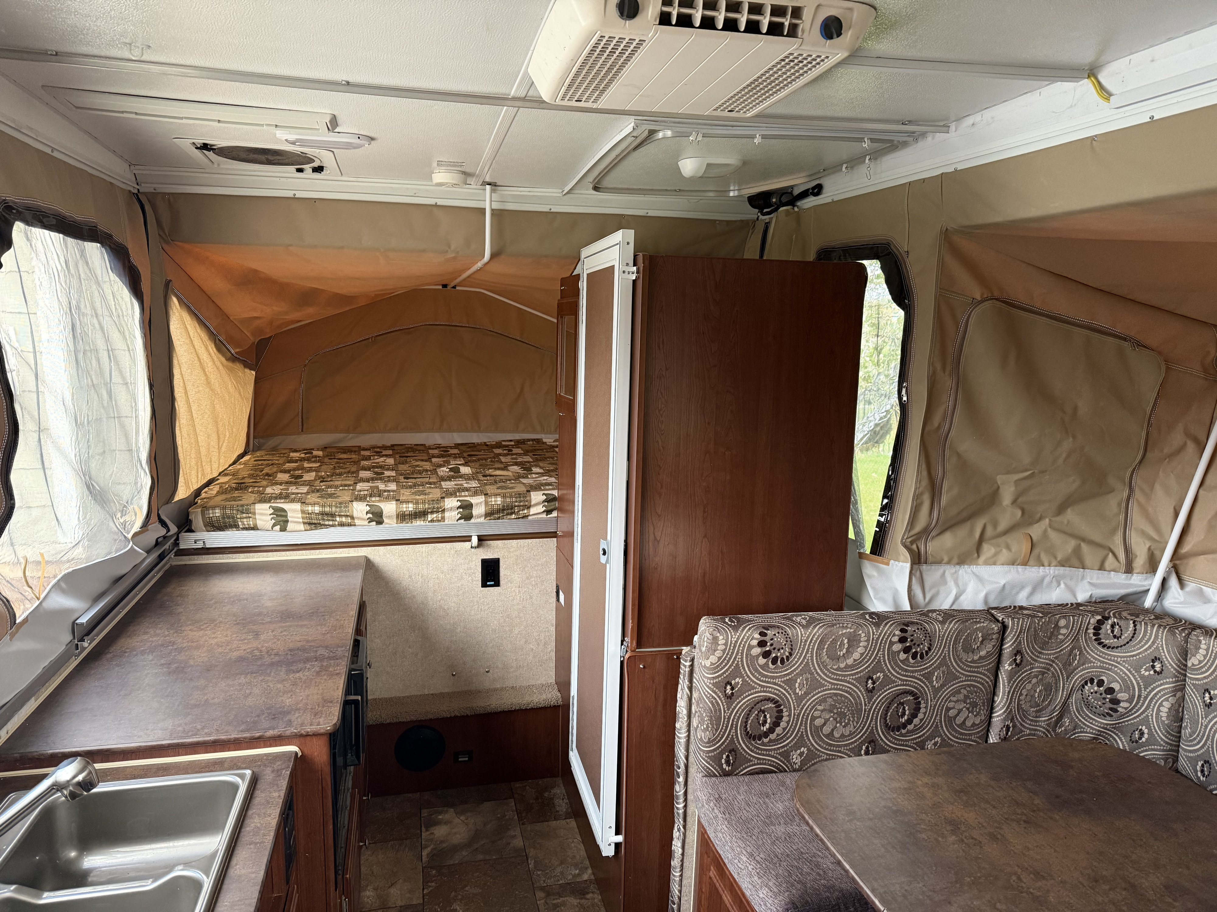 Inside a comfortable pop-up camper rv rental: cozy bed, functional kitchen, and dining area with patterned cushions.. Forest River Rockwood Premier 2014