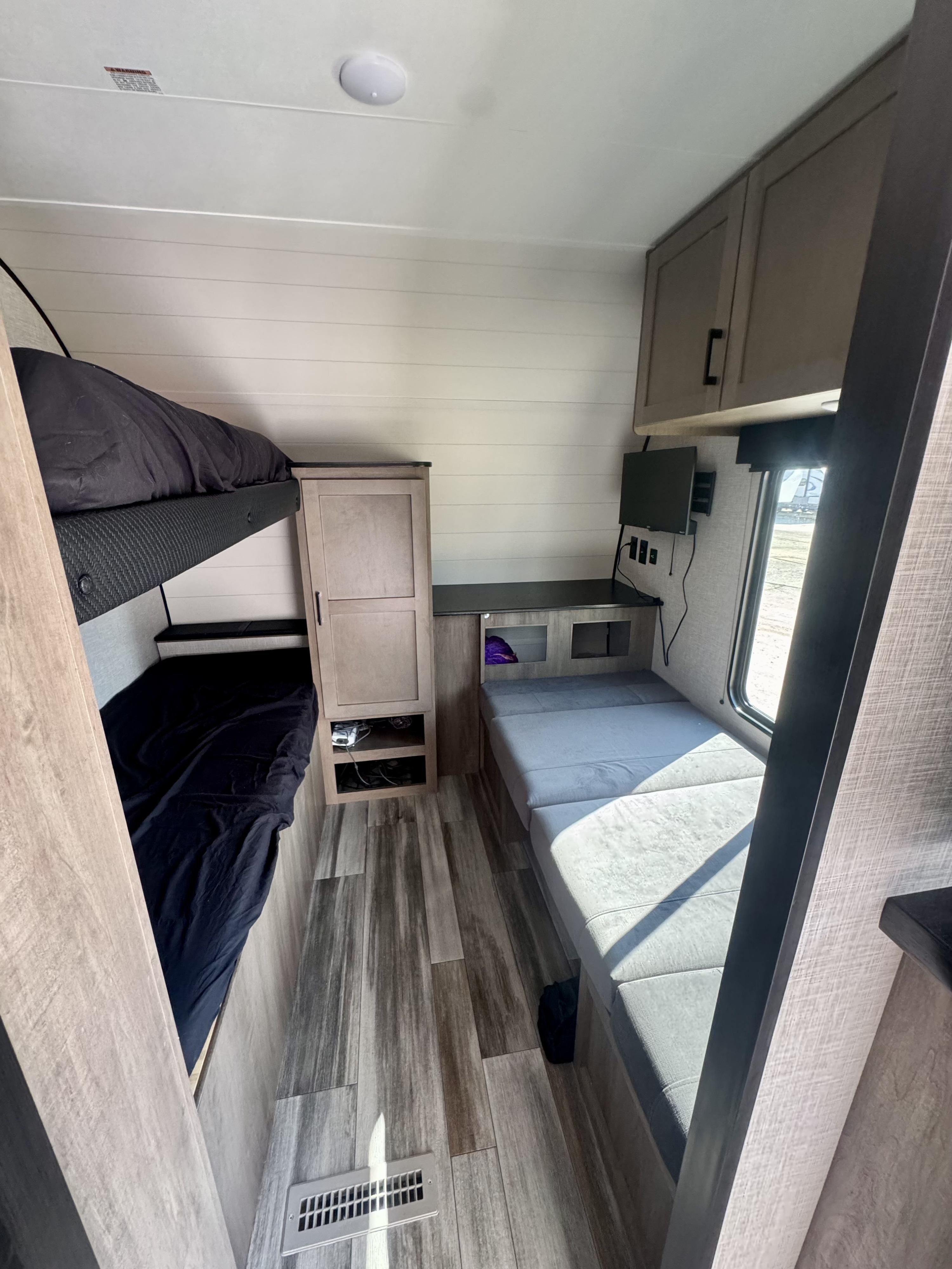 RV rental interior: bunk beds, dinette, and a small TV maximize space for comfortable travel. Wood-look floors & white walls.. Jayco Jay Flight SLX 2025