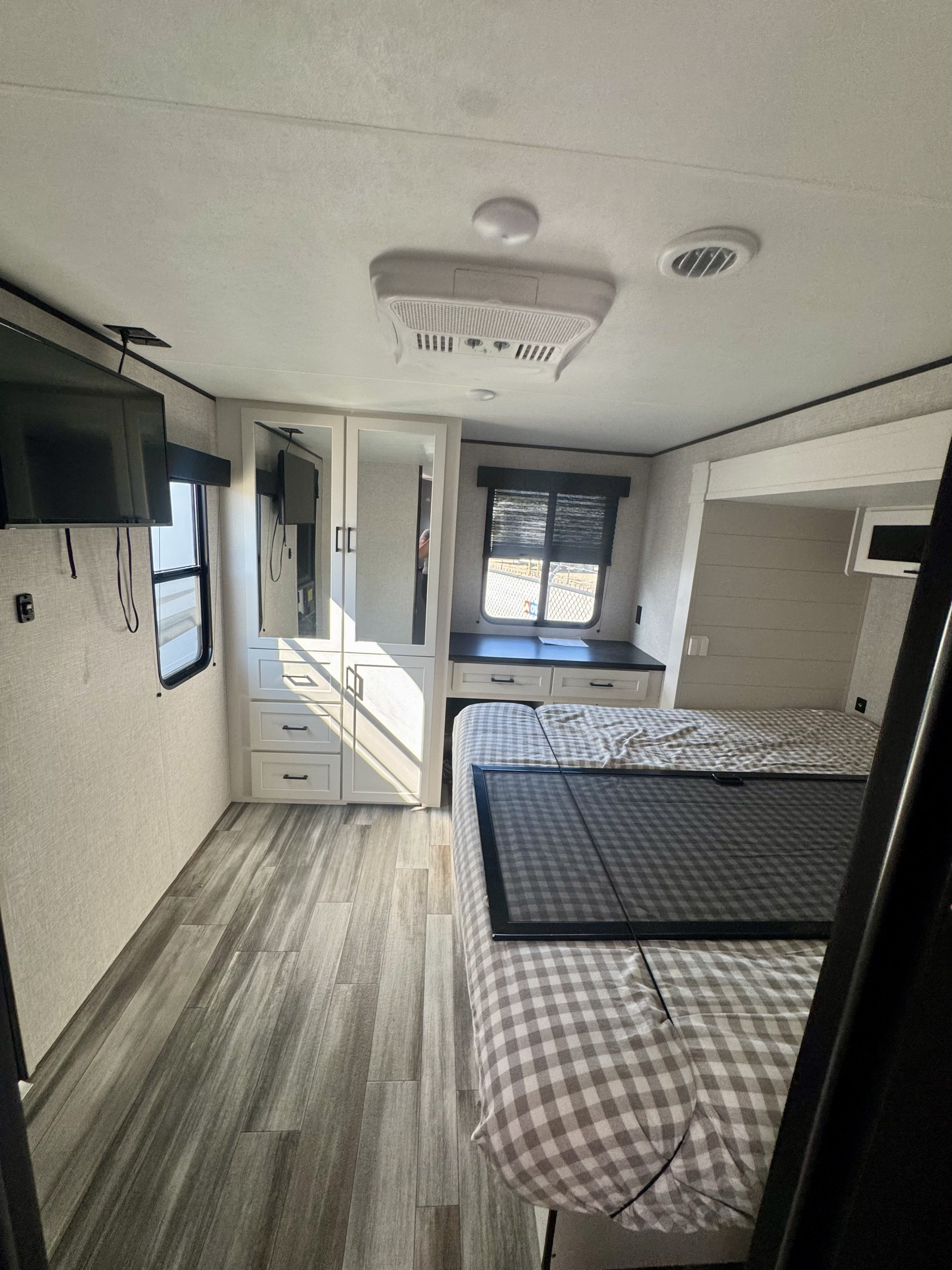 Inside an RV rental bedroom: cozy checkered bed, wood flooring, wardrobe, desk, TV, and window for your travels.. Jayco Jay Flight SLX 2025