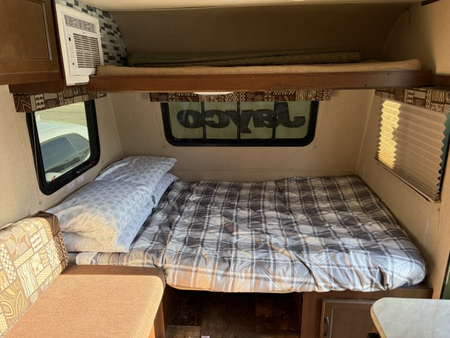 Cozy RV rental interior showing a main bed, upper bunk, dinette, and AC unit for comfortable travel.. Jayco Jay Flight SLX 2015