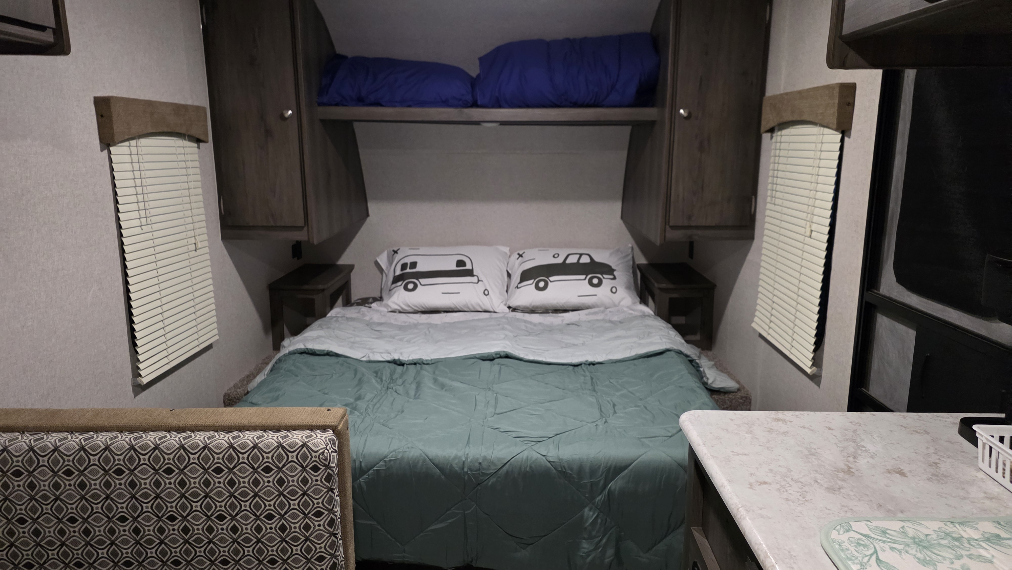 Cozy RV rental bedroom with teal/light blue bedding, car-themed pillows, bunk, overhead storage, and blinds.. Clipper Cadet 2020