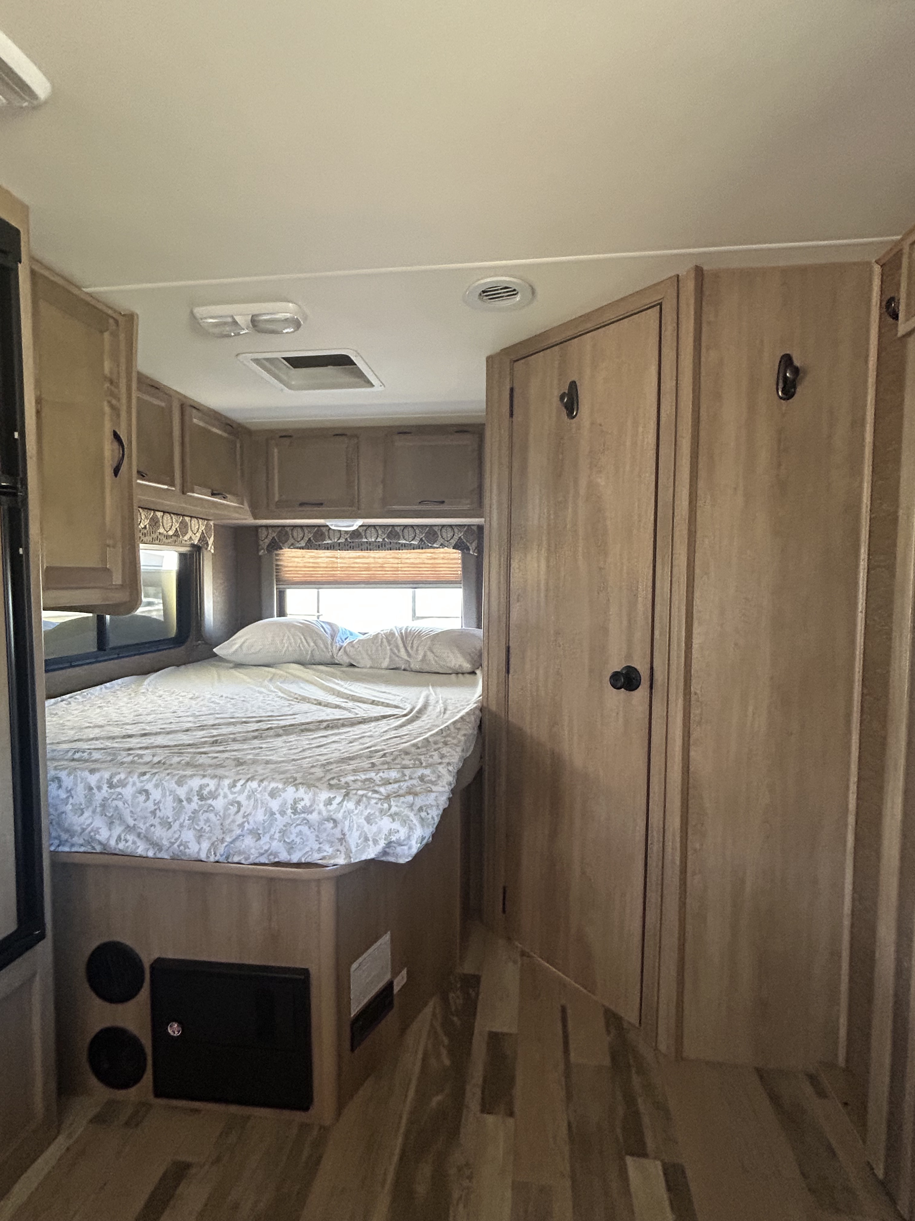 View inside an rv rental bedroom, showing a patterned bed, wood-toned cabinets, a door, and essential fixtures for mobile living.. Coachmen Freelander 2015