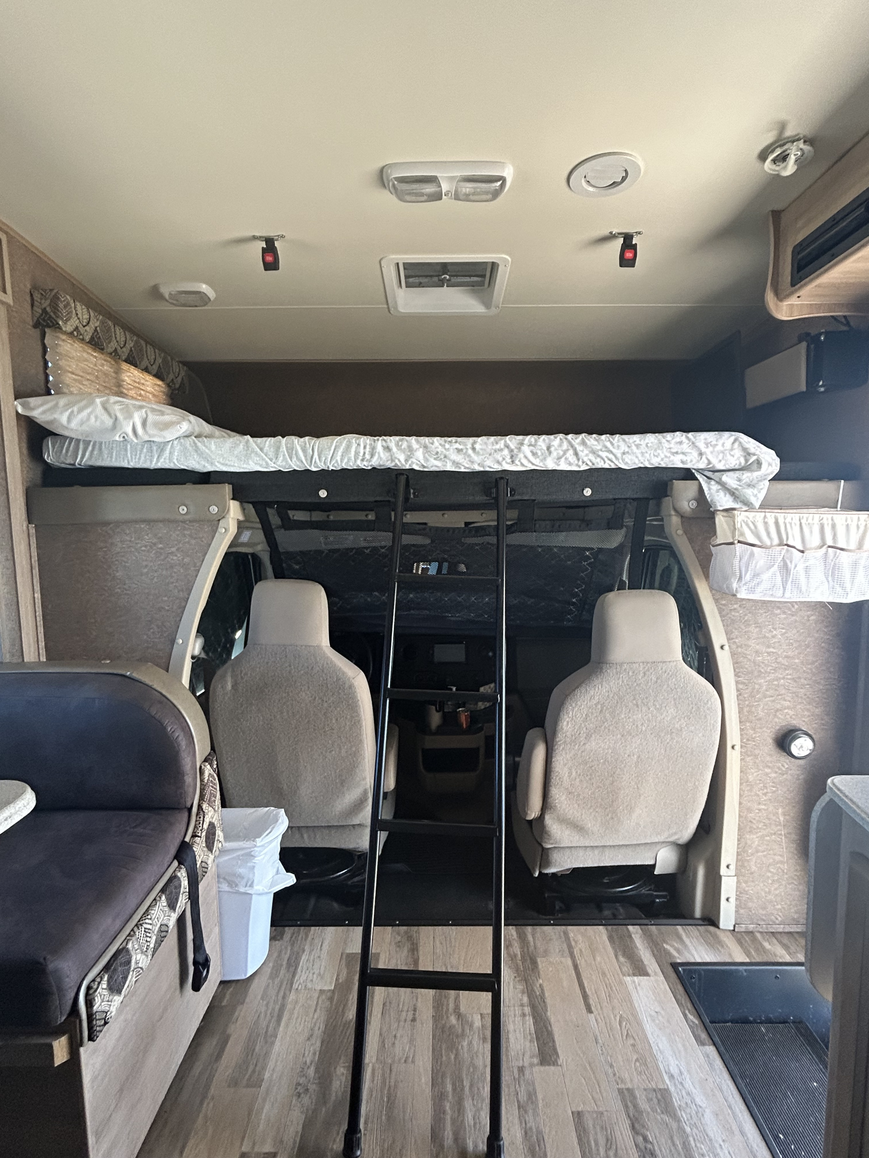 Rv rental interior featuring an over-cab bunk, ladder, driver/passenger seats, and dining booth with wood floor.. Coachmen Freelander 2015