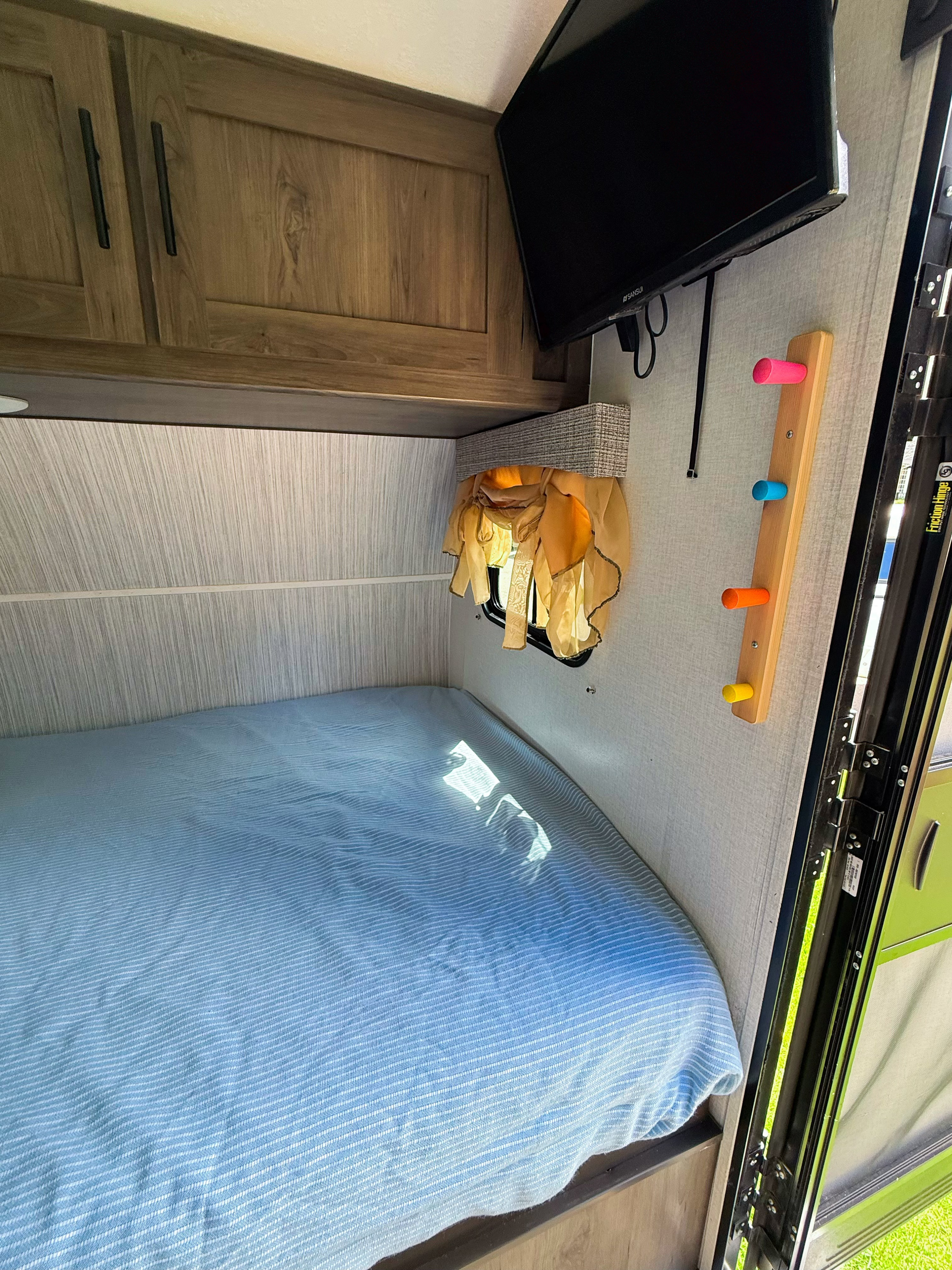 Cozy RV rental interior: bed, cabinets, TV, and a colorful peg rack, perfect for your camper adventure.. Coachmen 17BH 2022