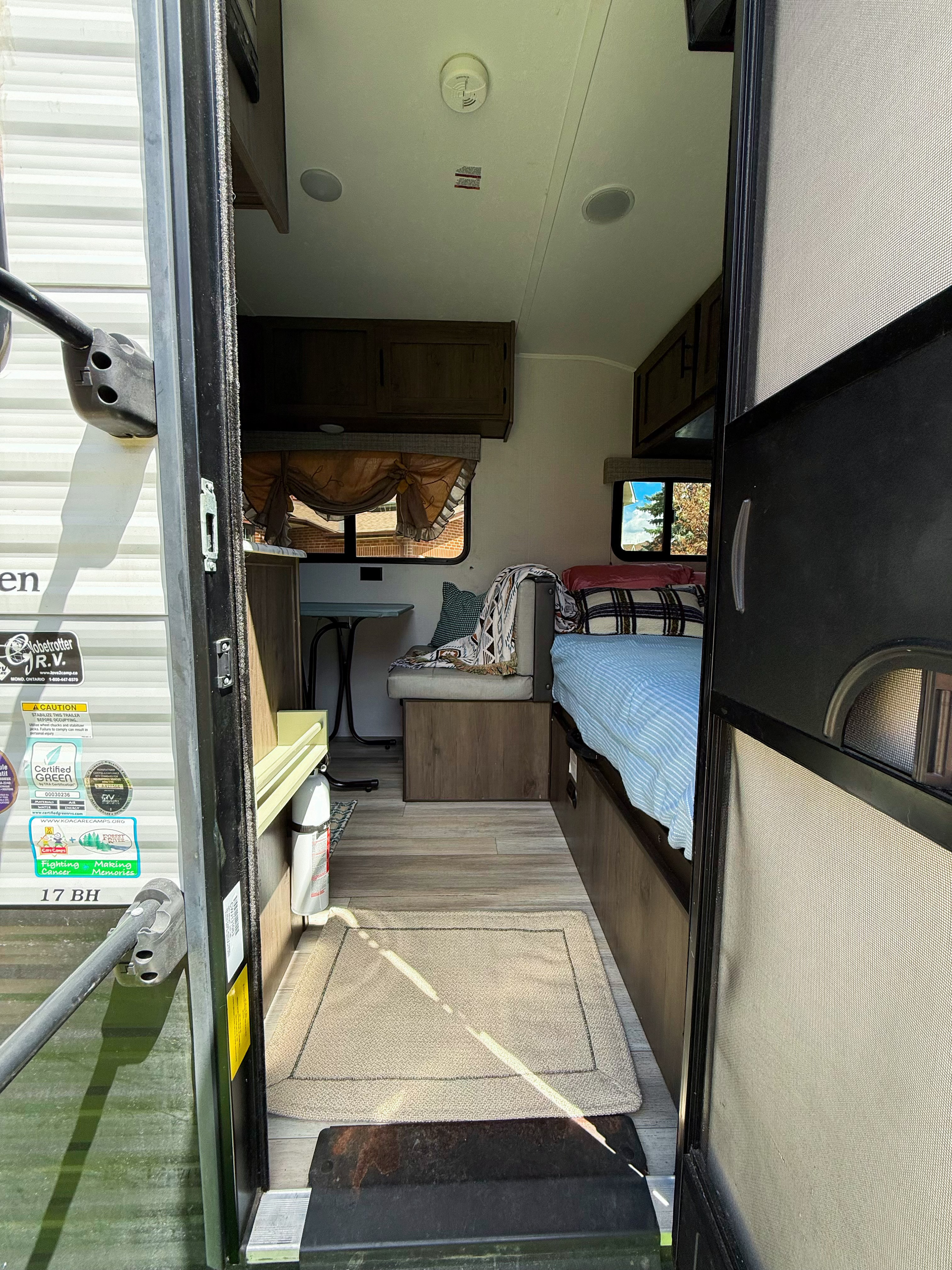 Step into this inviting rv rental! Interior view of a travel trailer with a bed, dinette, and fire extinguisher for safe camping.. Coachmen 17BH 2022