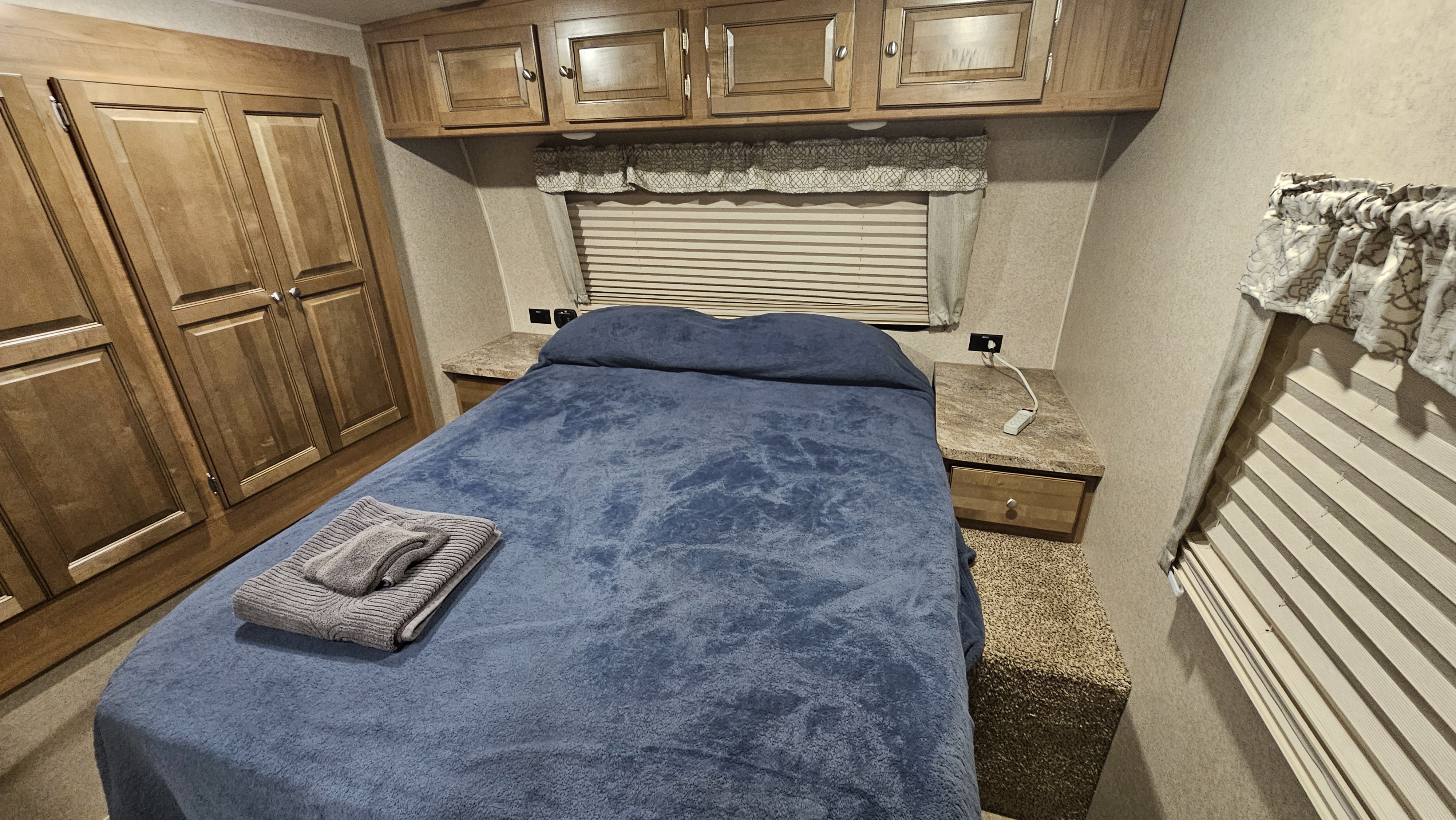 Cozy RV rental bedroom with a comfy bed, gray towels, overhead cabinets, and a wardrobe.. Forest River Rockwood Ultra Lite 2019