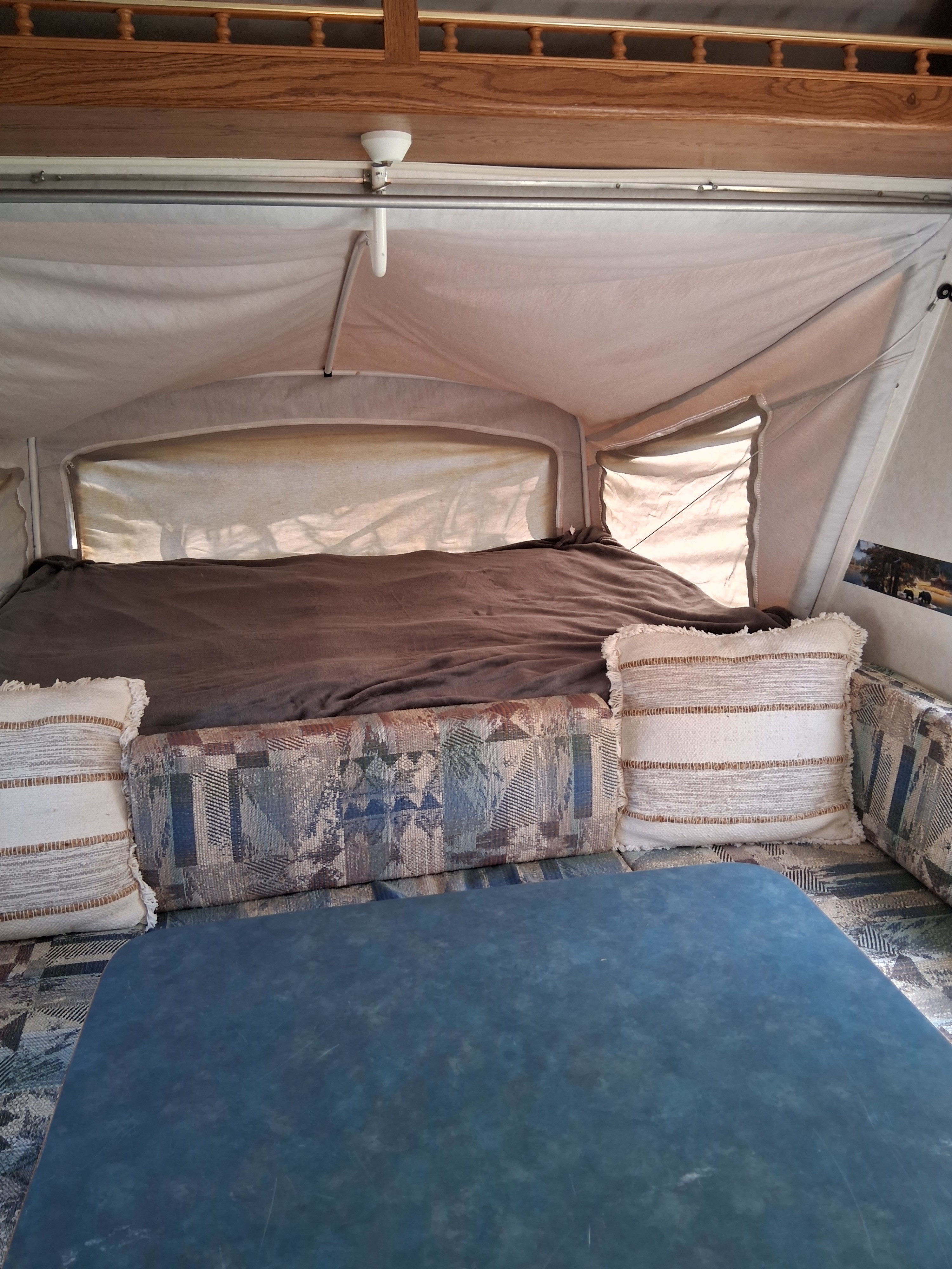 Pop-up RV rental interior: bed with brown blanket, patterned seating with pillows, and a blue table for a comfy stay.. Dutchmen Kodiak Cub 2000