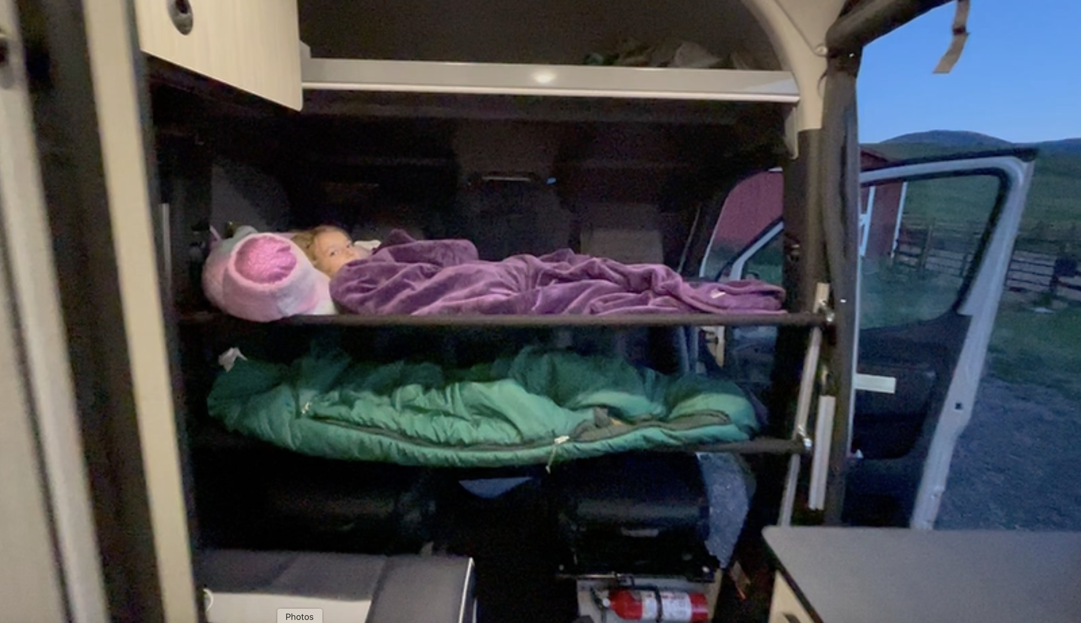 Cozy RV rental adventure: A child sleeps on an upper bunk inside a camper van, with a lower bunk and outdoor view visible.. Winnebago Revel 2022