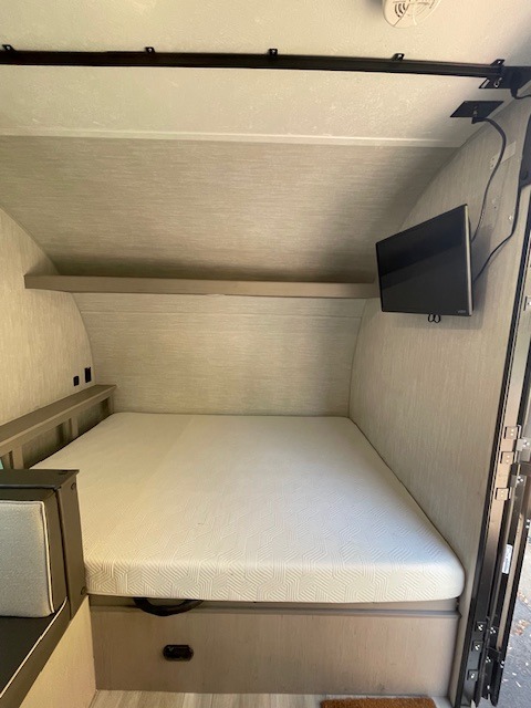 An RV rental's cozy bedroom, featuring a white mattress, wall-mounted TV, and built-in storage.. Coachmen Clipper 2025