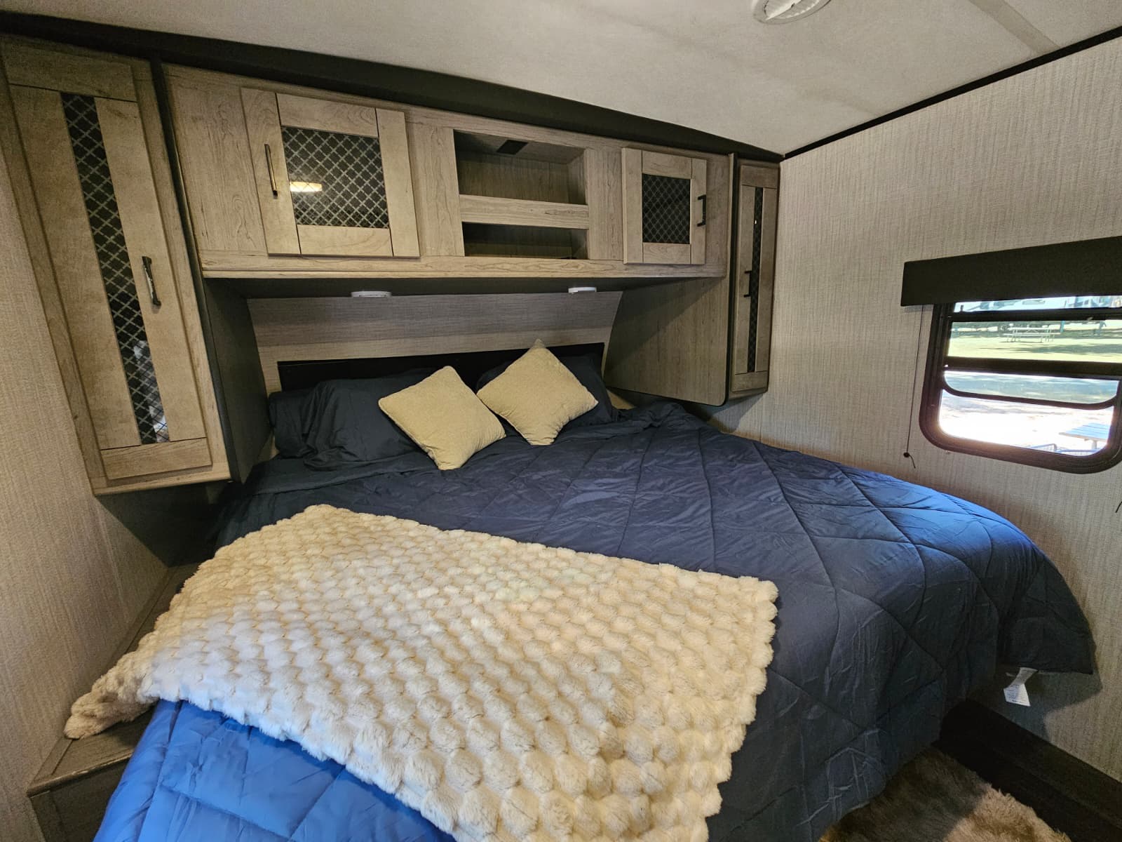 Cozy RV rental bedroom featuring a comfortable navy bed with a fluffy white blanket and overhead storage cabinets.. Heartland RVs Mallard 2021
