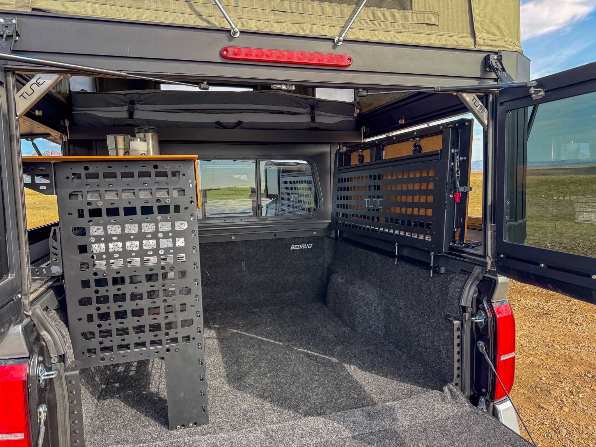 View inside an adventure-ready truck camper, perfect for an rv rental. Shows TUNE modular storage, BedRug liner, & cozy bed setup.. Toyota Tacoma 2026