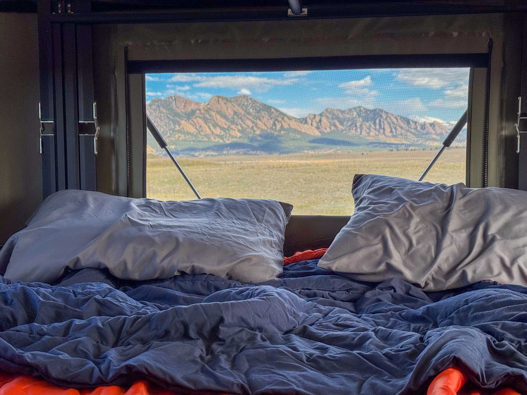 Cozy camper bed with a breathtaking mountain view. Perfect RV rental for scenic outdoor adventures.. Toyota Tacoma 2026