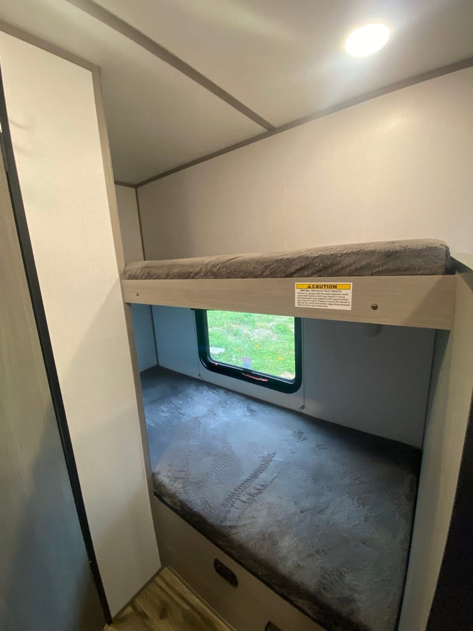 This RV rental features stacked bunk beds with mattresses and a window showing outdoor scenery. A cozy, compact sleeping area.. Dutchmen Coleman 2024