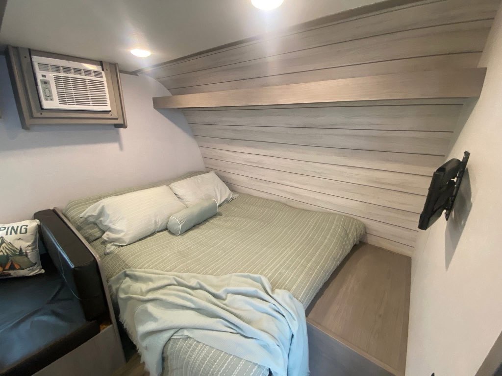 Inside an RV rental, discover this compact bedroom with a comfy bed, air conditioning, and wall-mounted TV bracket.. Dutchmen Coleman 2024