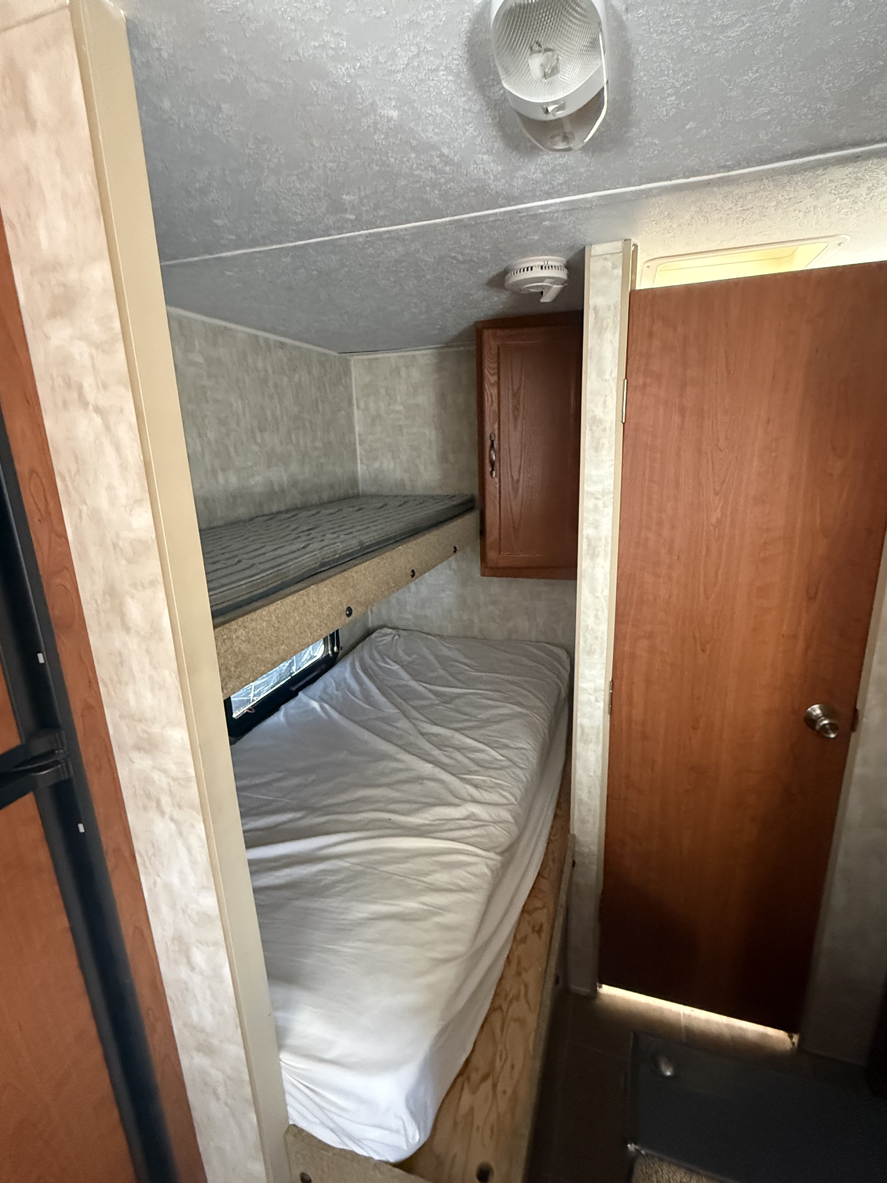 Compact rv rental interior showcasing two bunk beds, a storage cabinet, and a door, designed for efficient sleeping space.. Forest River Cherokee Grey Wolf 2010