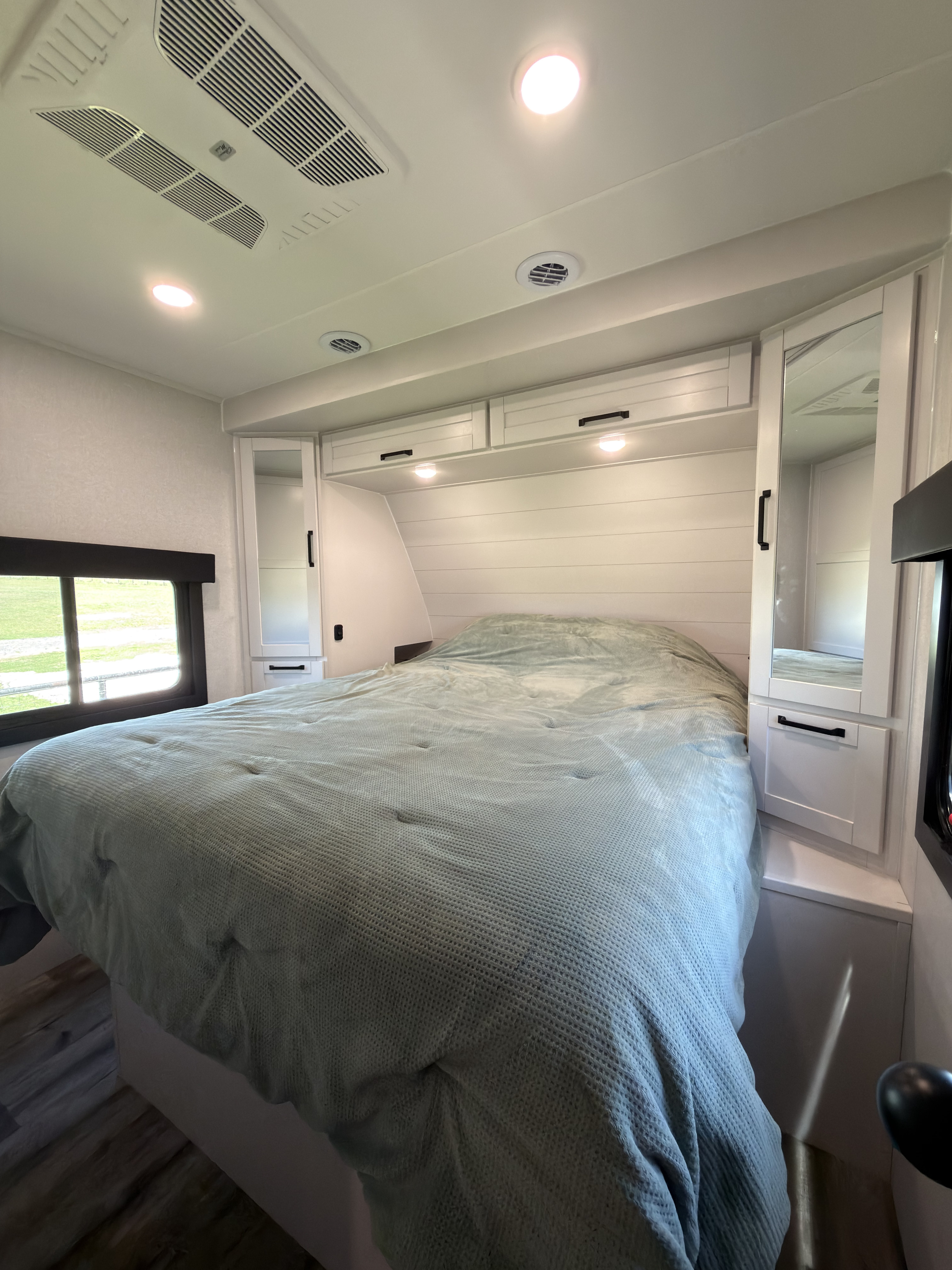 Bright RV rental bedroom with a light blue bed, white shiplap headboard, storage cabinets, and ceiling vents/lights.. Highland Ridge RV Open Range Roamer 2026