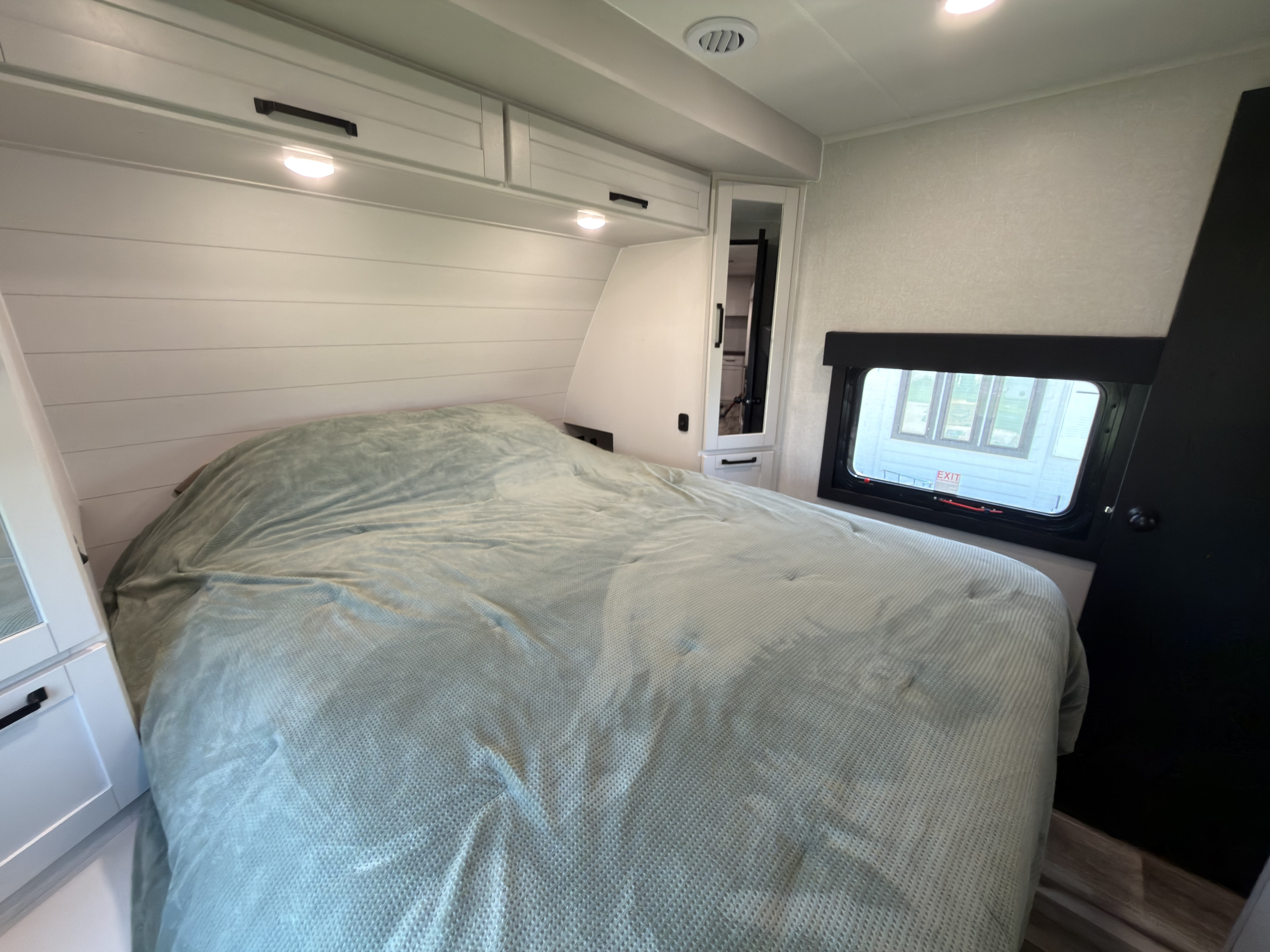 Explore this comfortable RV rental bedroom, featuring a light green bed, white cabinets, and a window with an emergency exit.. Highland Ridge RV Open Range Roamer 2026