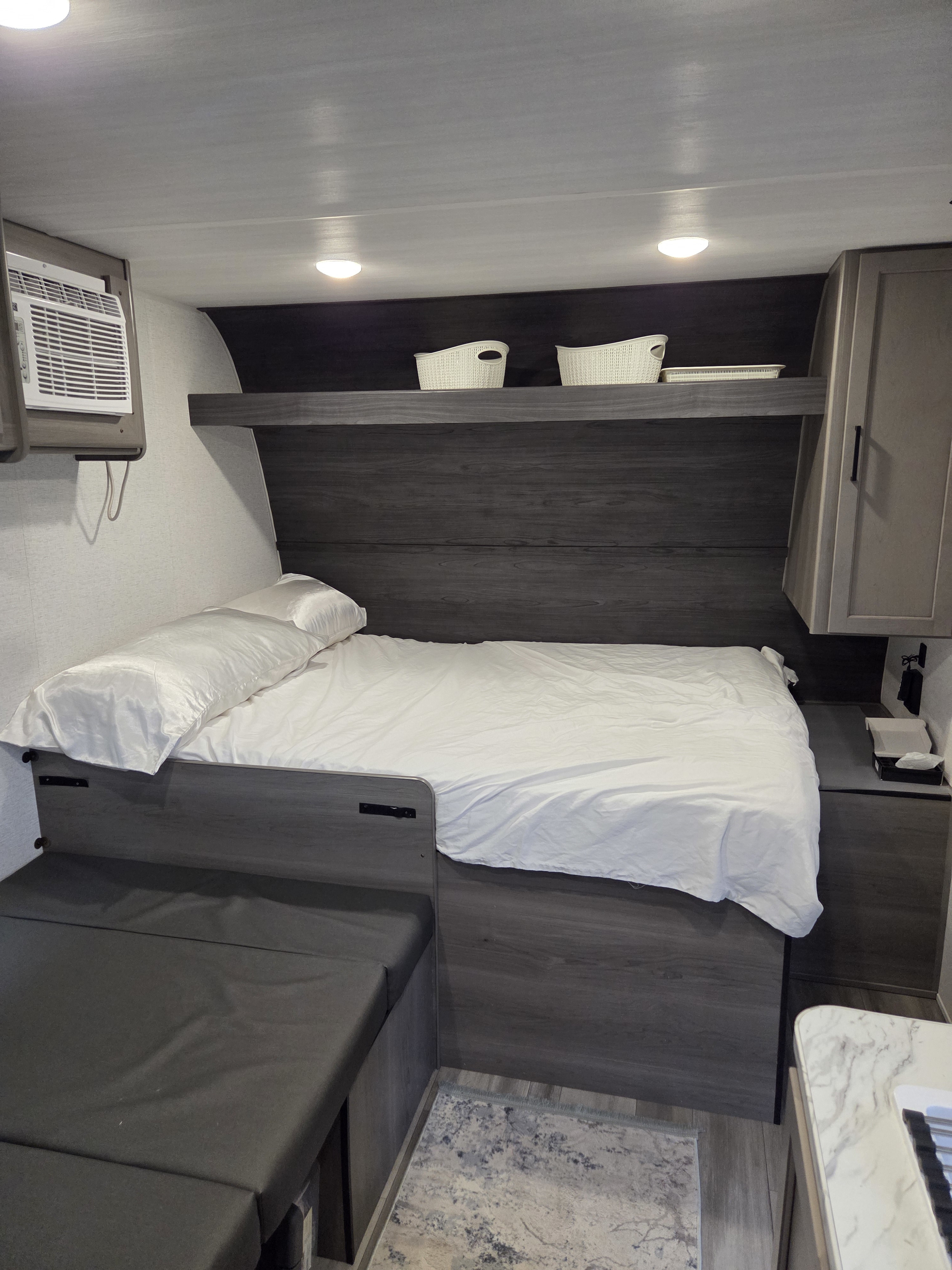 Inside an RV rental, a cozy bedroom with a bed, AC unit, overhead storage, and convertible dinette seating.. Keystone RV Hideout Sport 2024
