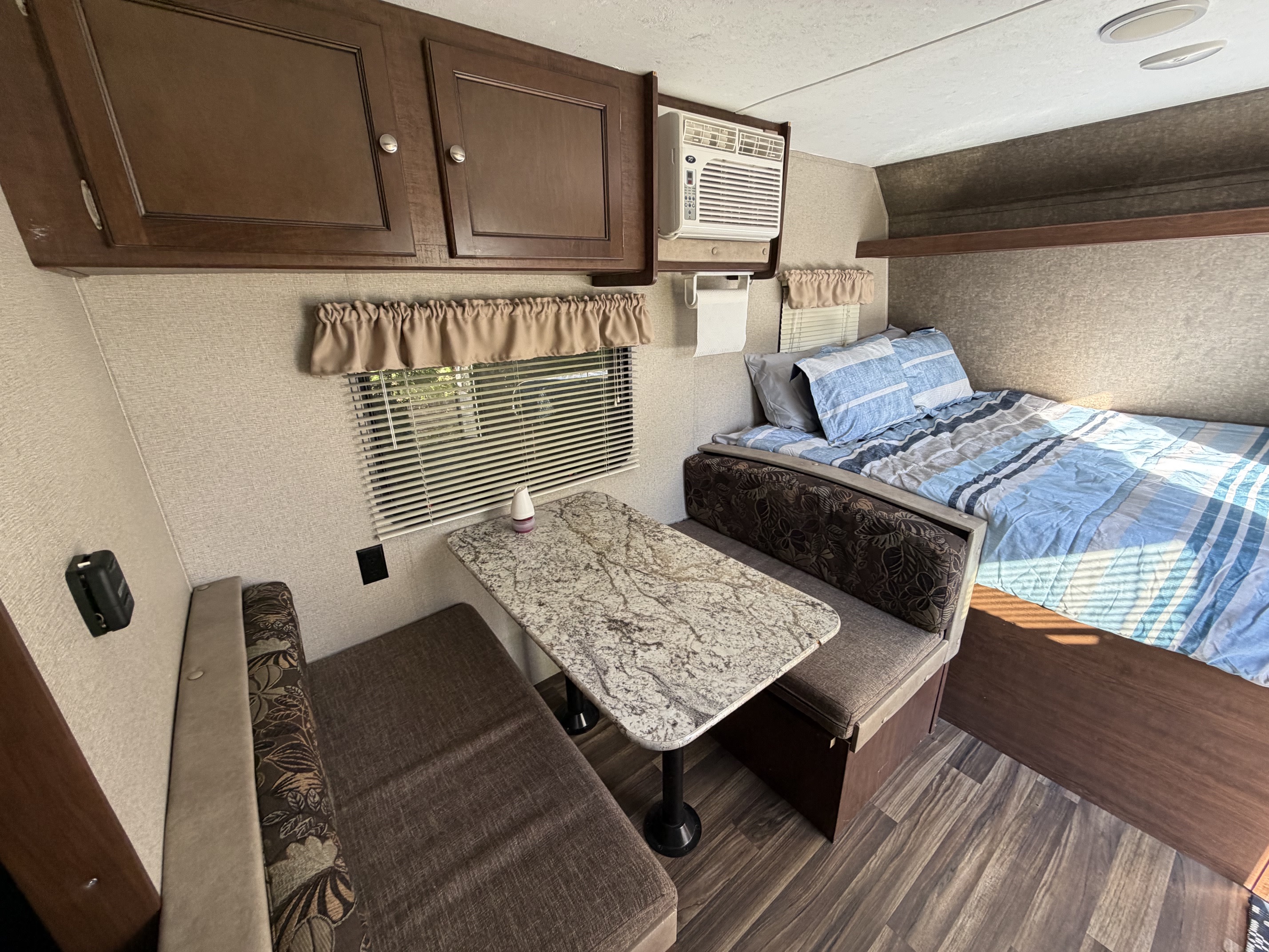 Cozy RV rental interior featuring a dinette, comfortable bed, overhead cabinets, and a window AC unit.. Keystone RV Hideout LHS 2018