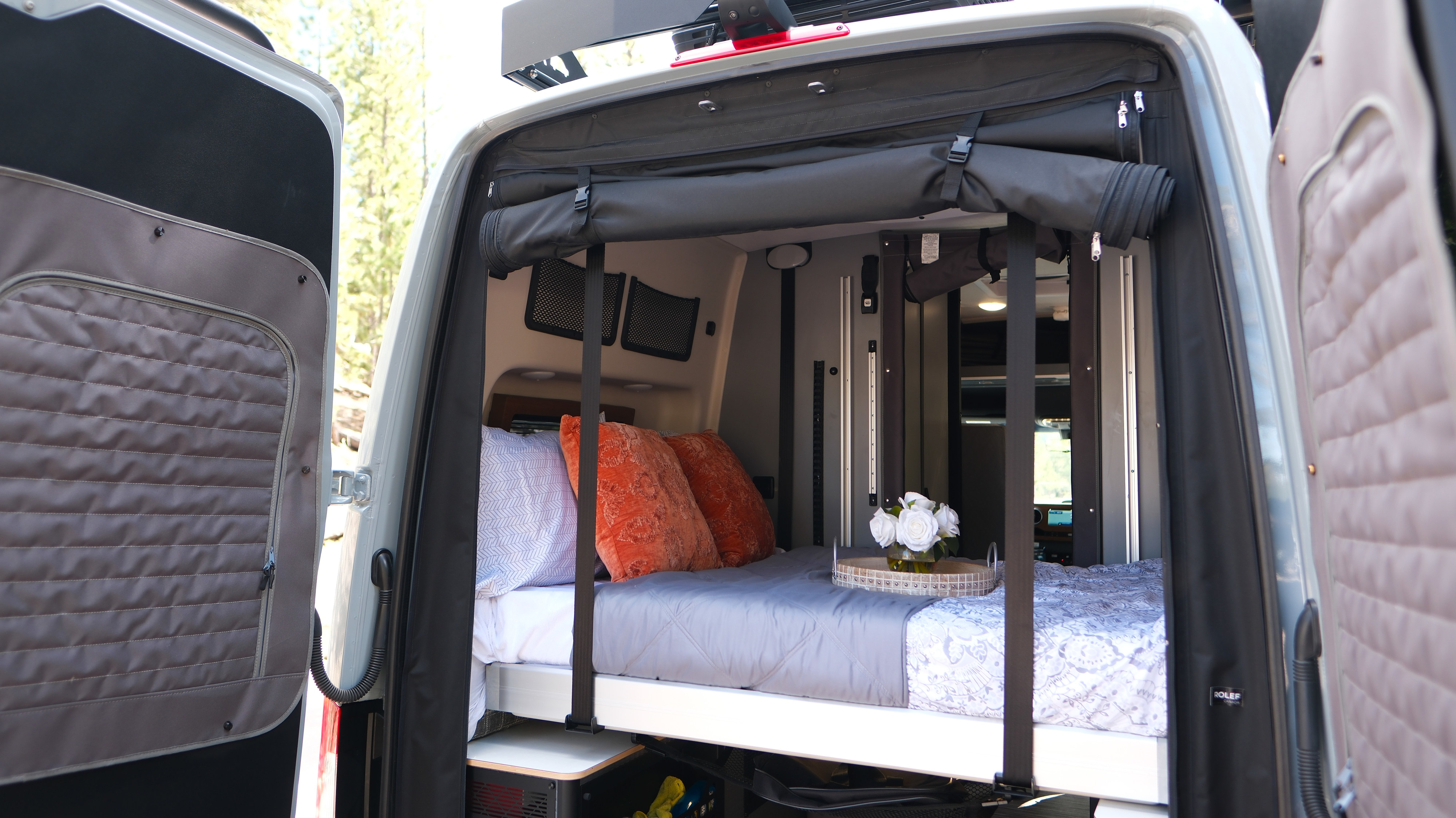 Cozy RV rental bed in a camper van with open rear doors revealing nature. Perfect for van life travel.. Mercedes Winnebago 2026
