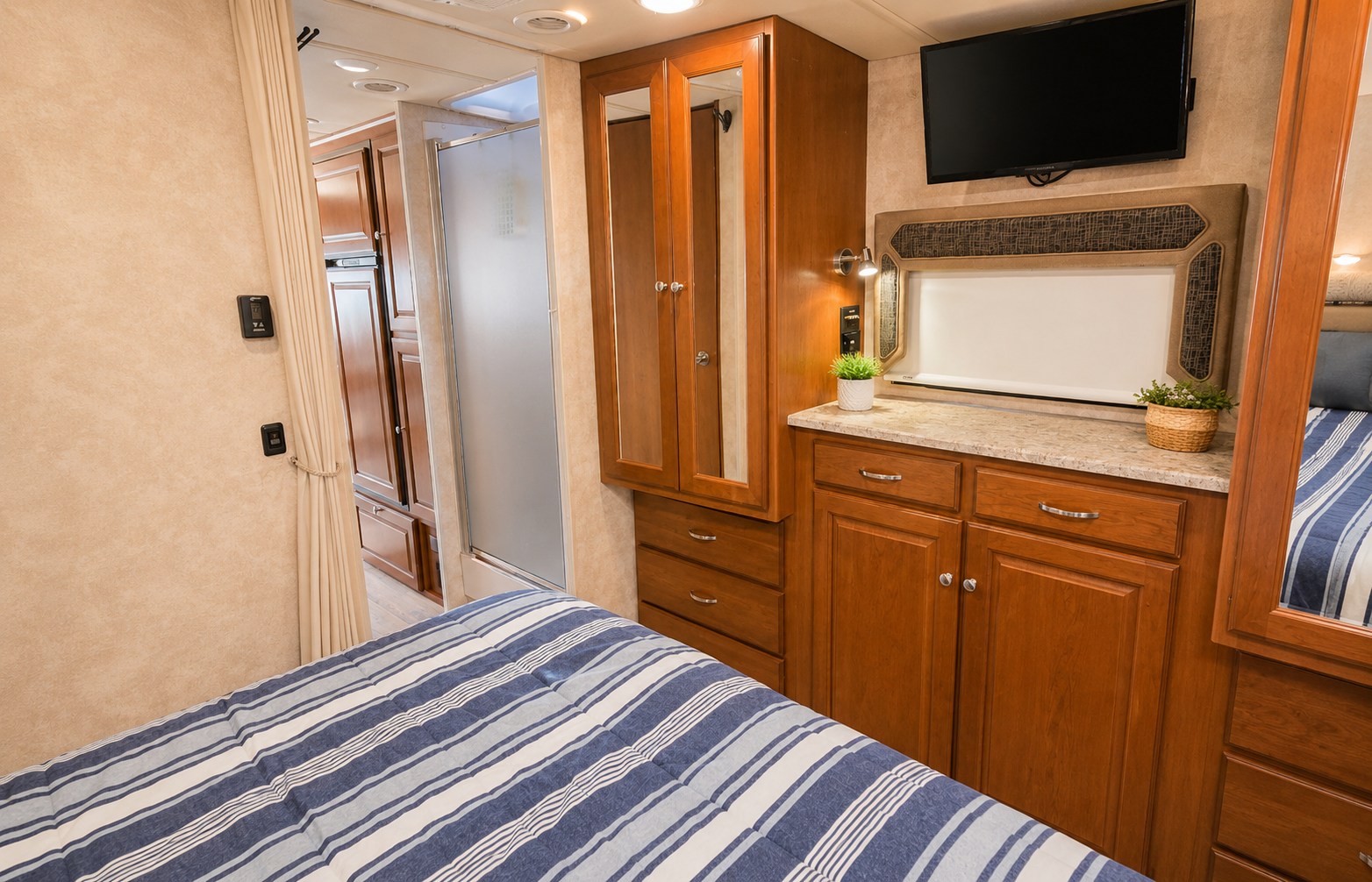 Comfortable RV rental interior: cozy bedroom with a striped bed, built-in cabinetry, TV, and a compact bathroom.. Winnebago Vista LX 2019