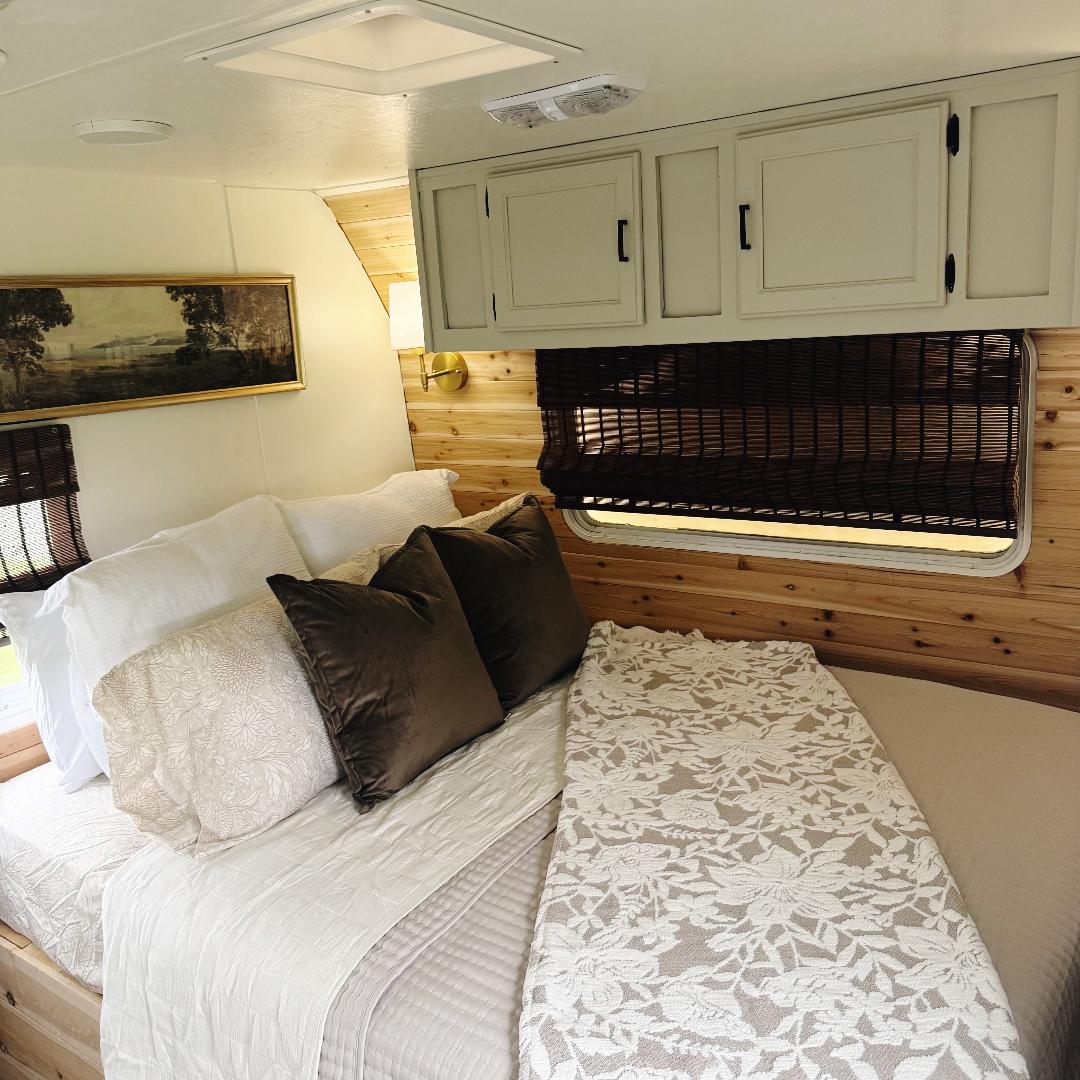 Cozy renovated RV rental bedroom featuring warm wood walls, plush bedding, modern overhead cabinets, and a serene atmosphere.. Keystone RV Sprinter 2000