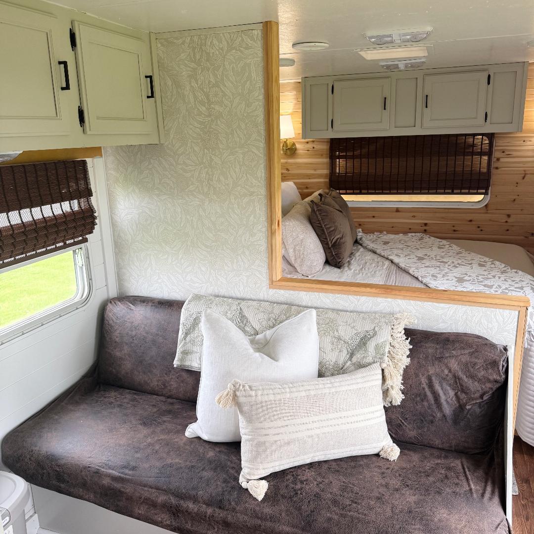 Cozy RV rental interior: a dark brown couch with pillows, a botanical wallpapered wall, and a peek into the bed area.. Keystone RV Sprinter 2000