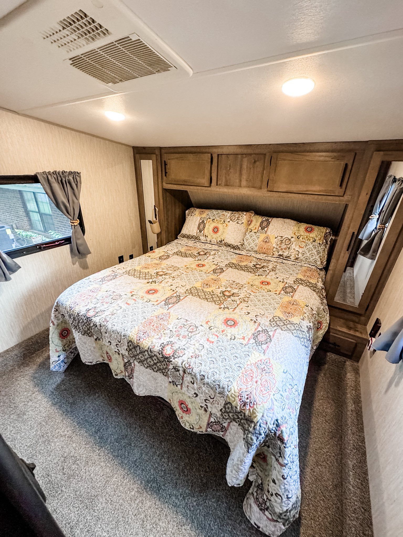 Cozy RV rental bedroom with a queen bed, patterned quilt, overhead storage, window, and AC unit for comfortable travel.. Forest River Cherokee Wolf Pack 2020