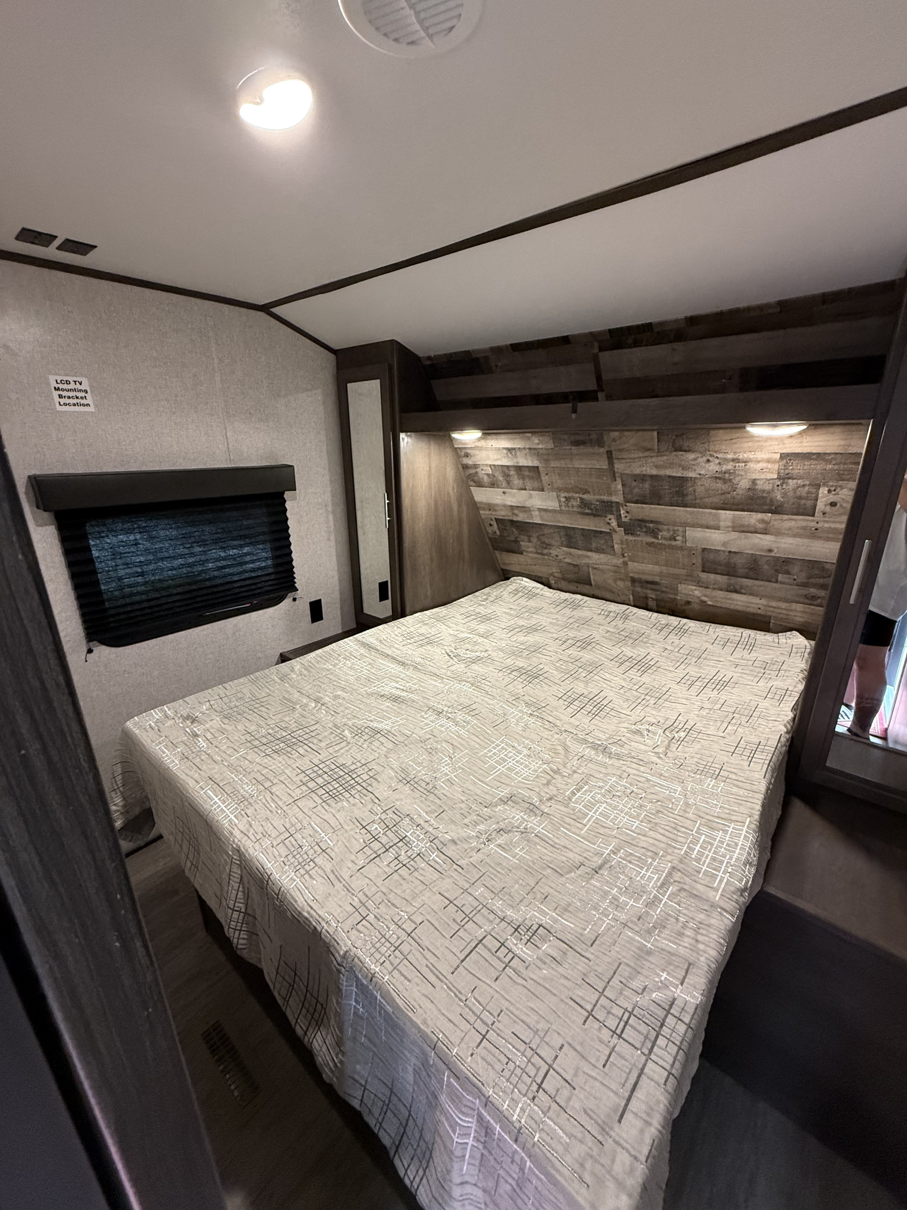 Inviting RV rental bedroom: queen bed with rustic headboard, window, built-in storage with mirror, and ceiling lights.. Aspen Trail Aspen Trail Trailer 2021