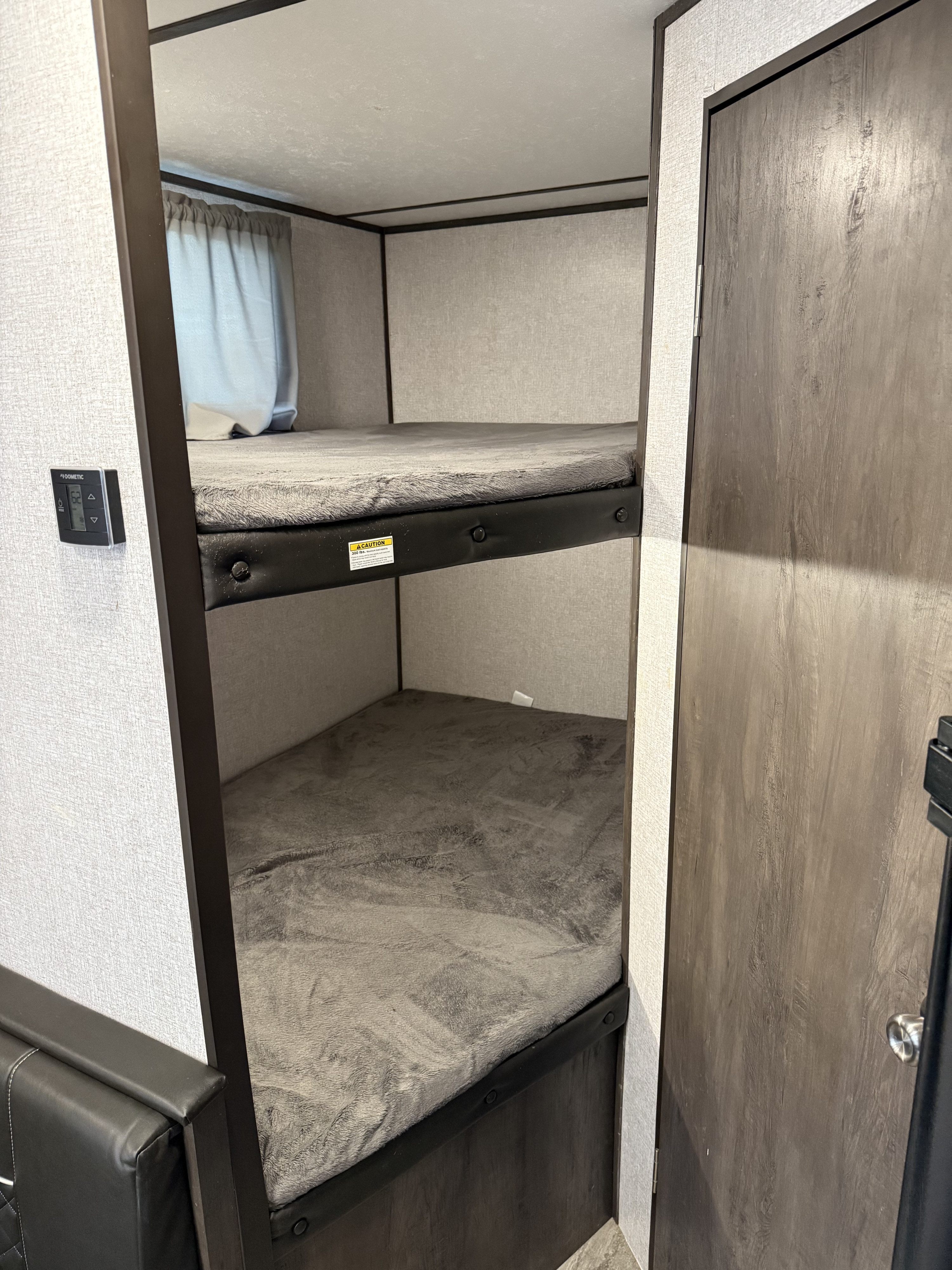 Cozy RV rental bunk beds with gray blankets, wall controls, and a wooden door, offering comfortable sleeping space.. Aspen Trail Aspen Trail Trailer 2021