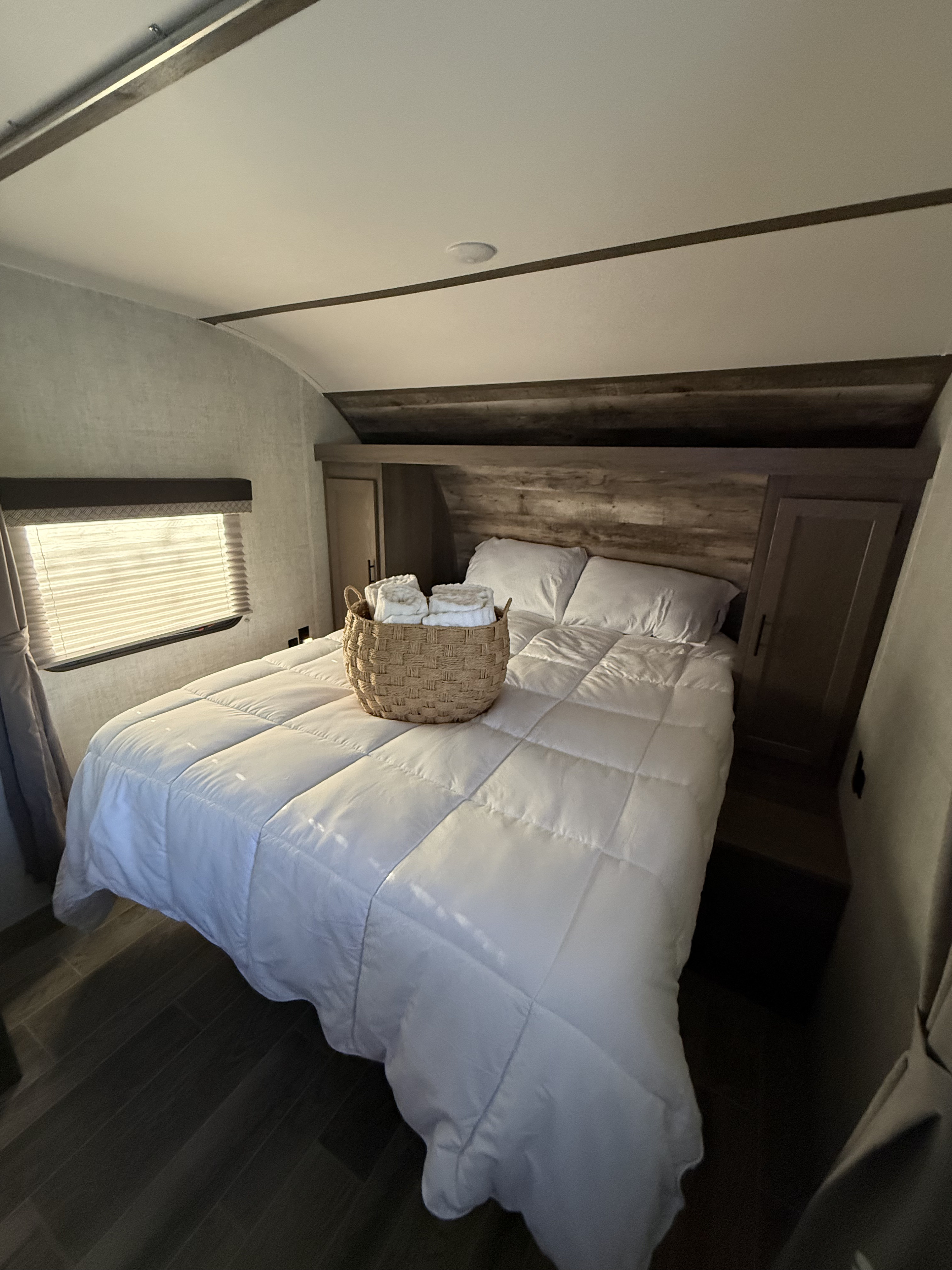 Cozy RV rental bedroom with a comfortable bed, white bedding, and a basket of fresh towels. Features modern wood accents.. Gulf Stream Ameri-Lite 2021